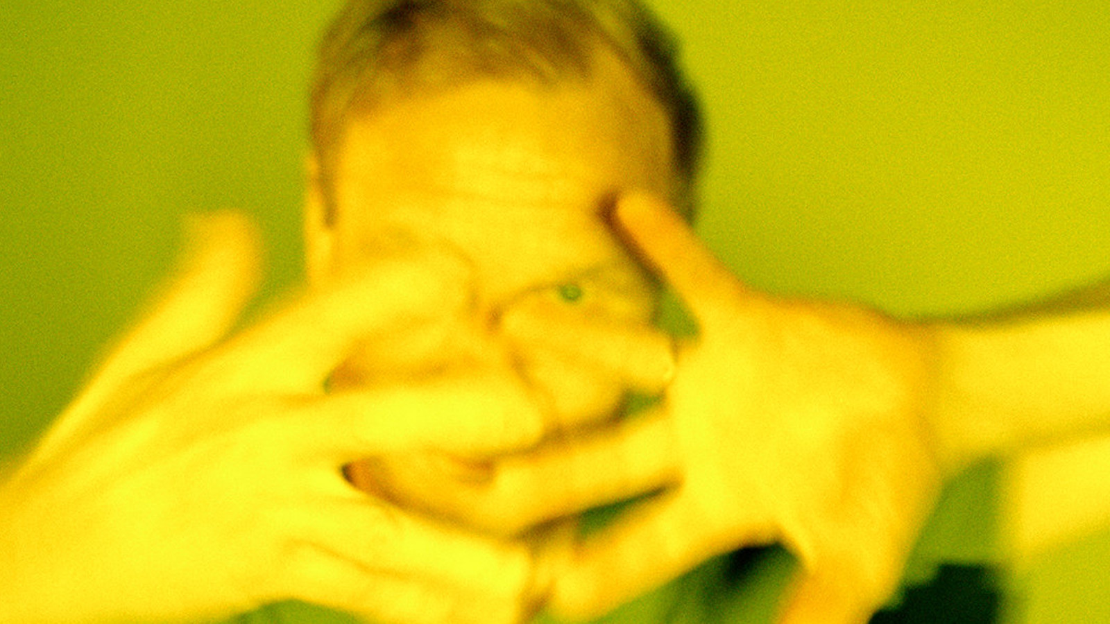 Kuvassa on Ismo Alanko kasvokuvassa ja hänellä on sormet haristettuna kasvojen edessä. Kuvan sävy on vihertävä.