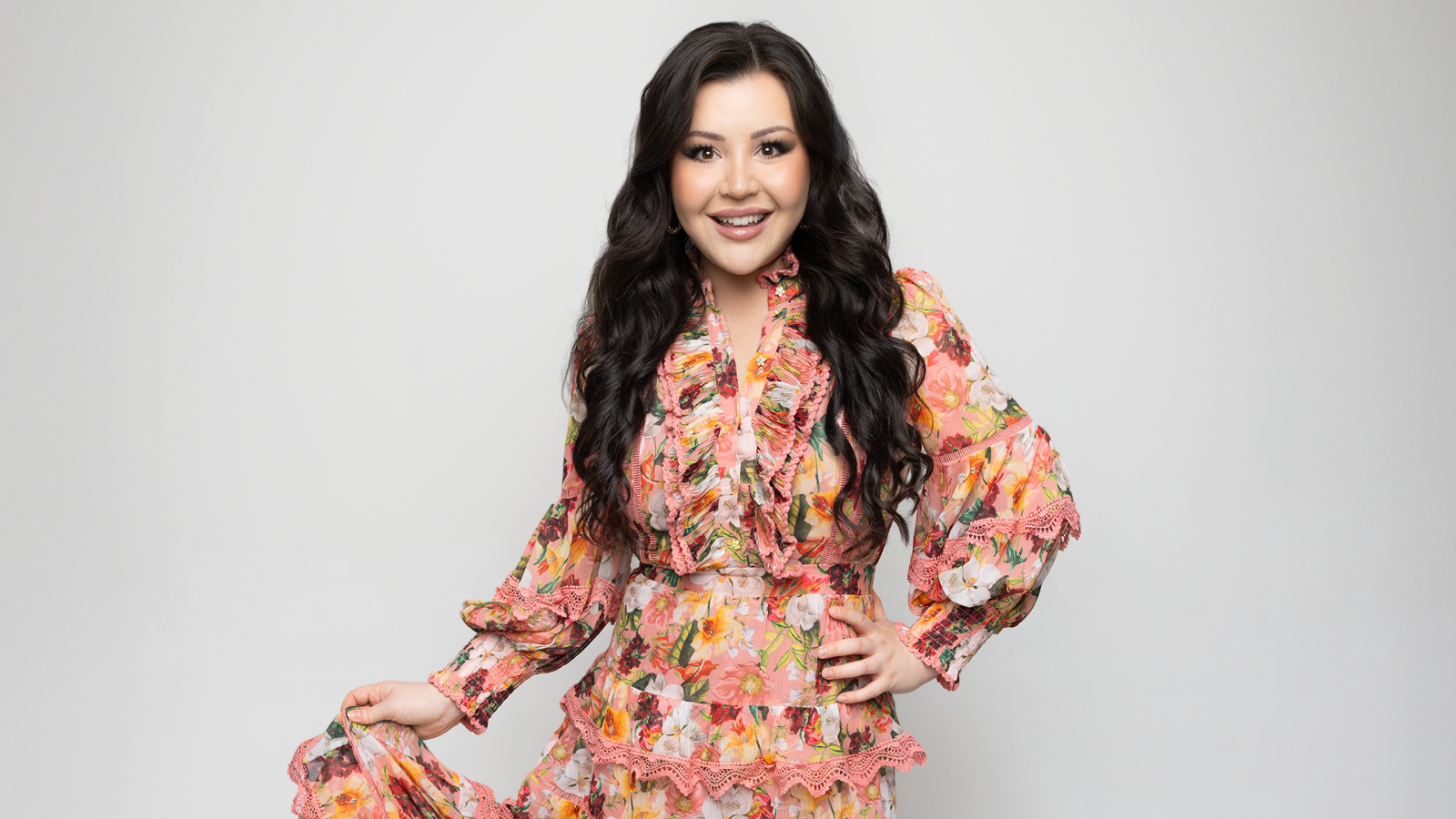 Kuvassa on Diandra seisomassa ja nänellä on vaalean roosa mekko, jossa on kukkakuvioita. Hä pitää oikealla kädellään helmasta kiinni.