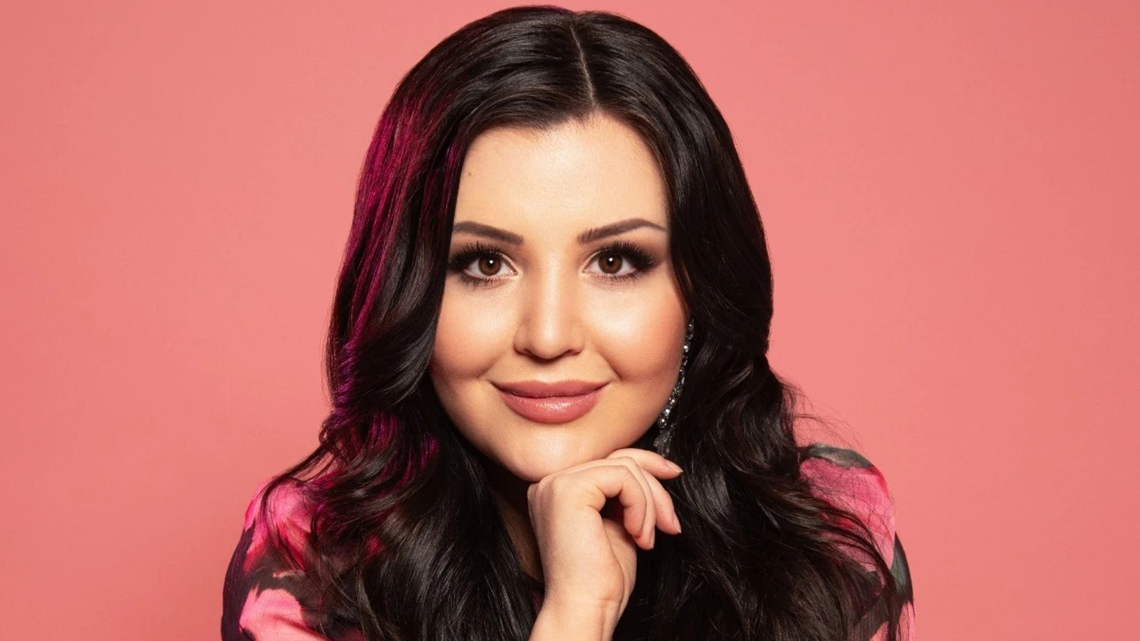 Kuvassa on Diandra kasvokuvassa ja hänellä on oikea käsi leuan alla. Tausta on roosa.