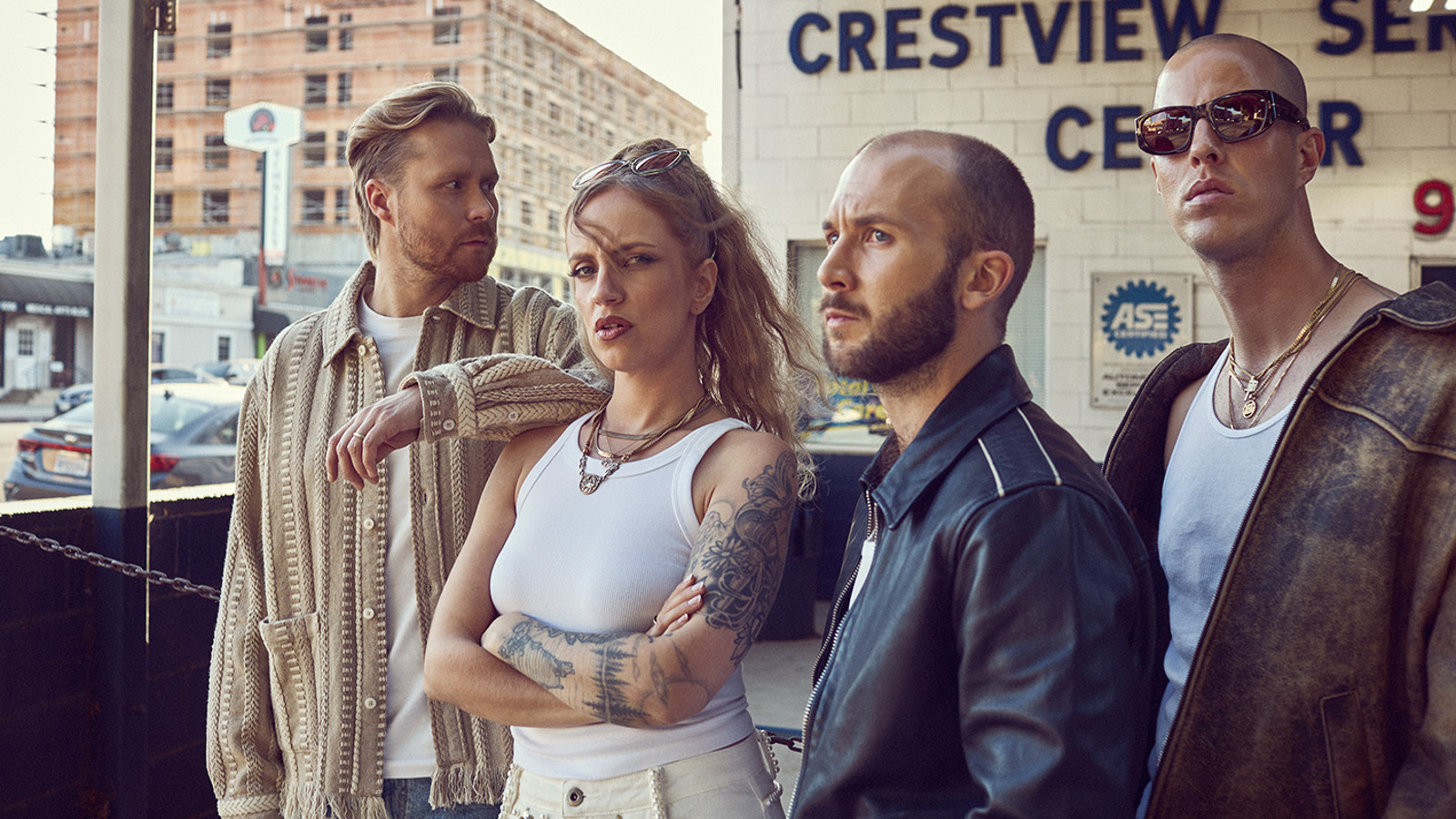 Kuvassa on Haloo Helsingin jäsenet seisomassa tilassa, jossa lukee seinässä Crestview Center. Vasemmalla on mies vaalean ruskeassa villatakissa vieressäänElli valkoisessa hihattomassa t-paidassa. Oikealla on kaksi miestä ja heillä on tummat takit päällään. Lasi-ikkunan takaa näkyy vaalean ruskea iso kerrostalo.