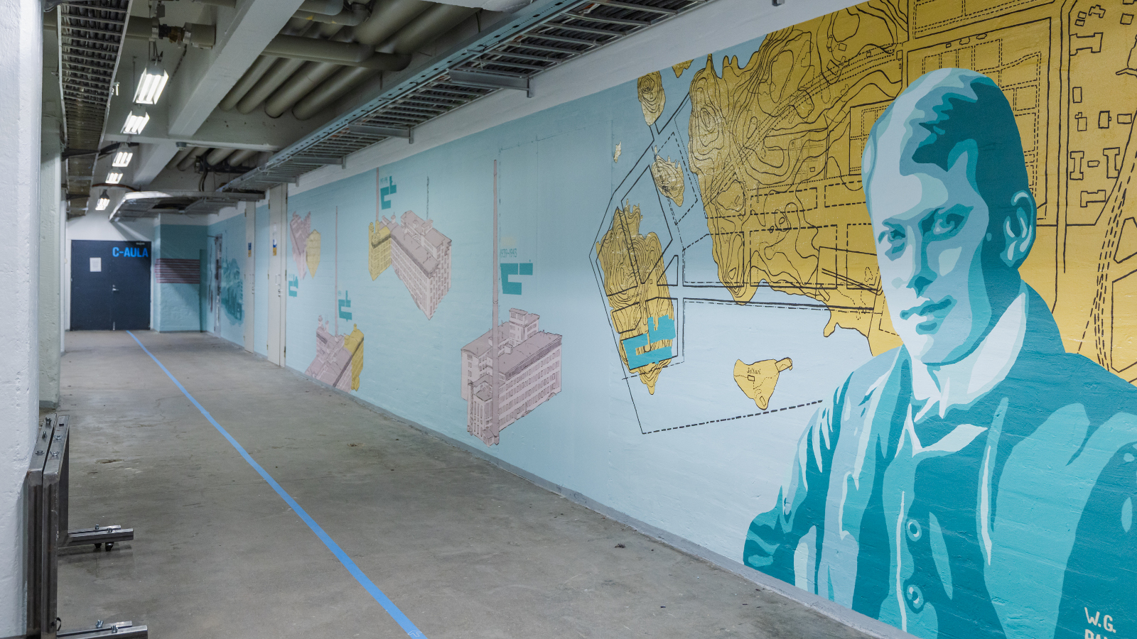 Kuvassa on käytävä, jossa on oikean puoleinen seinä ja sen pohja on vaalean sininen.  Seinällä on karttapohjamaisia kuvioita ja oikealla keltainen niemi.  Lähinnä oikealla on iso miehen rintakuva vaalean sinisessä takissa.