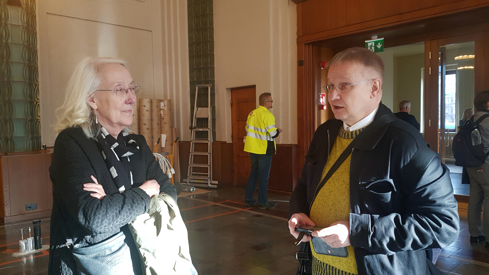 Kuvassa ovat vasemmalla Pirjo Huvila tummassa villatakissa ja oikealla Mikko Mannberg tummassa takissa ja kellertävässä puserossa. He ovat puolivartalokuvassa.