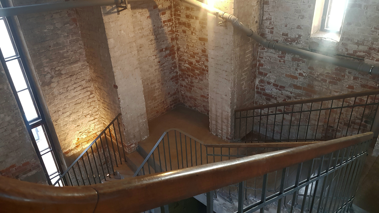 Kuvassa on kellotornin portaikkoa ja siinä näkyy portaikon ruskeaa kaidetta ja tiiliseinää sekä kaksi harmaata pylvästä sekä pystyikkuna.