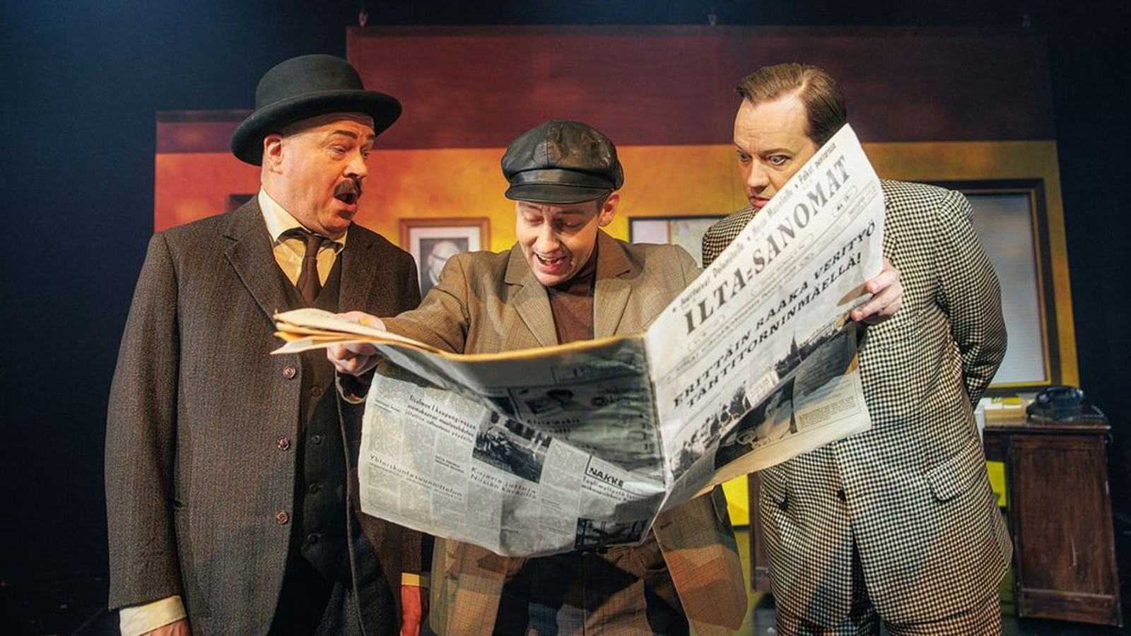Kuvassa on seisomassa vasemmalla vanhempi mies knalli päässään ja ruskeassa takissa.  Hänen vieressään oikealla on vaalean ruskeassa takissa lukemassa Iltasanomia hämmästyneenä.  Oikealla on vaaleassa pikkuruudullisessa takissa oleva mies katsoo myös lehteä.