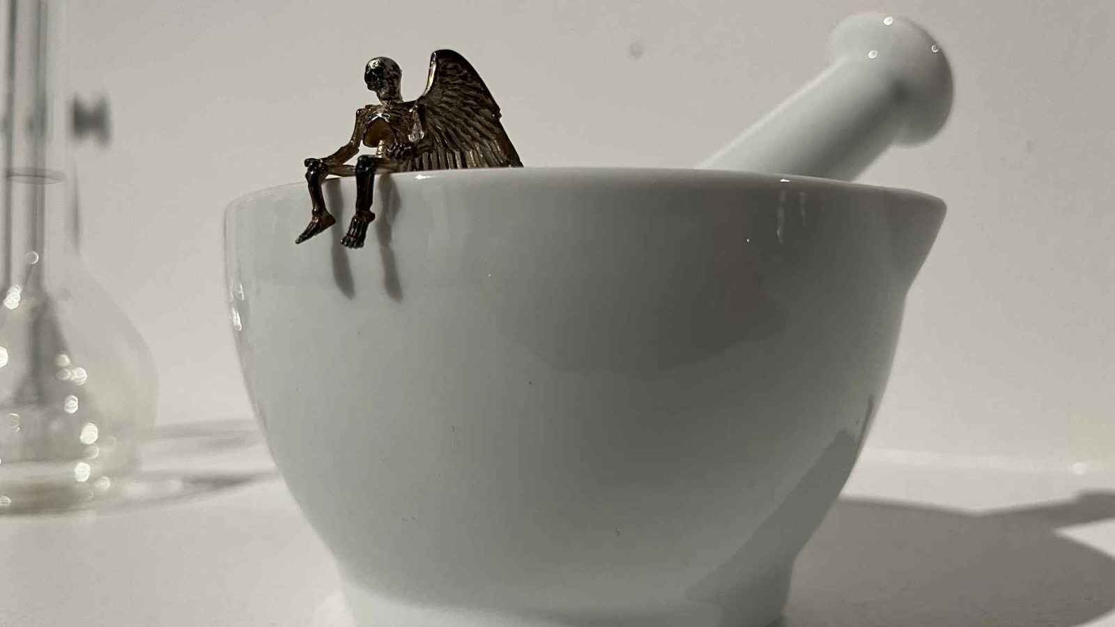 Kuvassa on vaalea huhmarekulho ja siinä huhmare. Reunalla istuu pieni musta enkeli, jolla roikkuu jalat kulhon reunan yli.