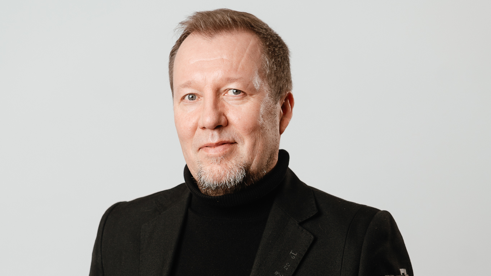 Kuvassa on Mikko Korsulainen kasvokuvassa. Hänellä on musta korkeakauluksinen paika päällään.