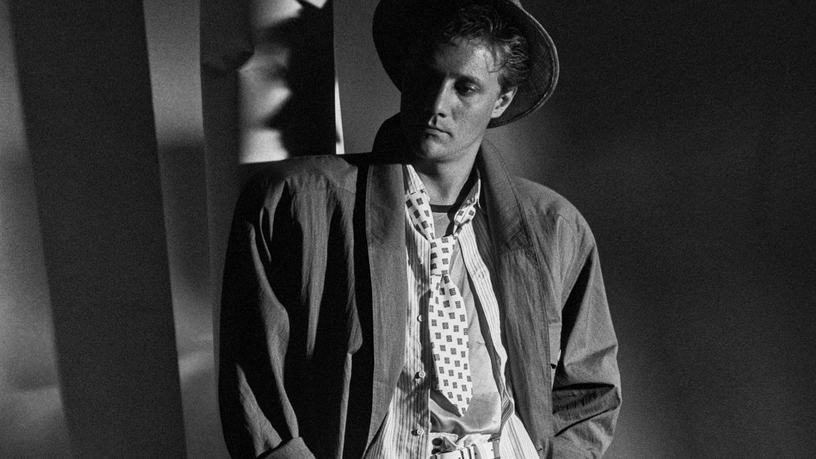 Kuvassa on nuori mies lierihatussa ja väljässä takissa ja paidassa. Kuva on musta-valkoinen.