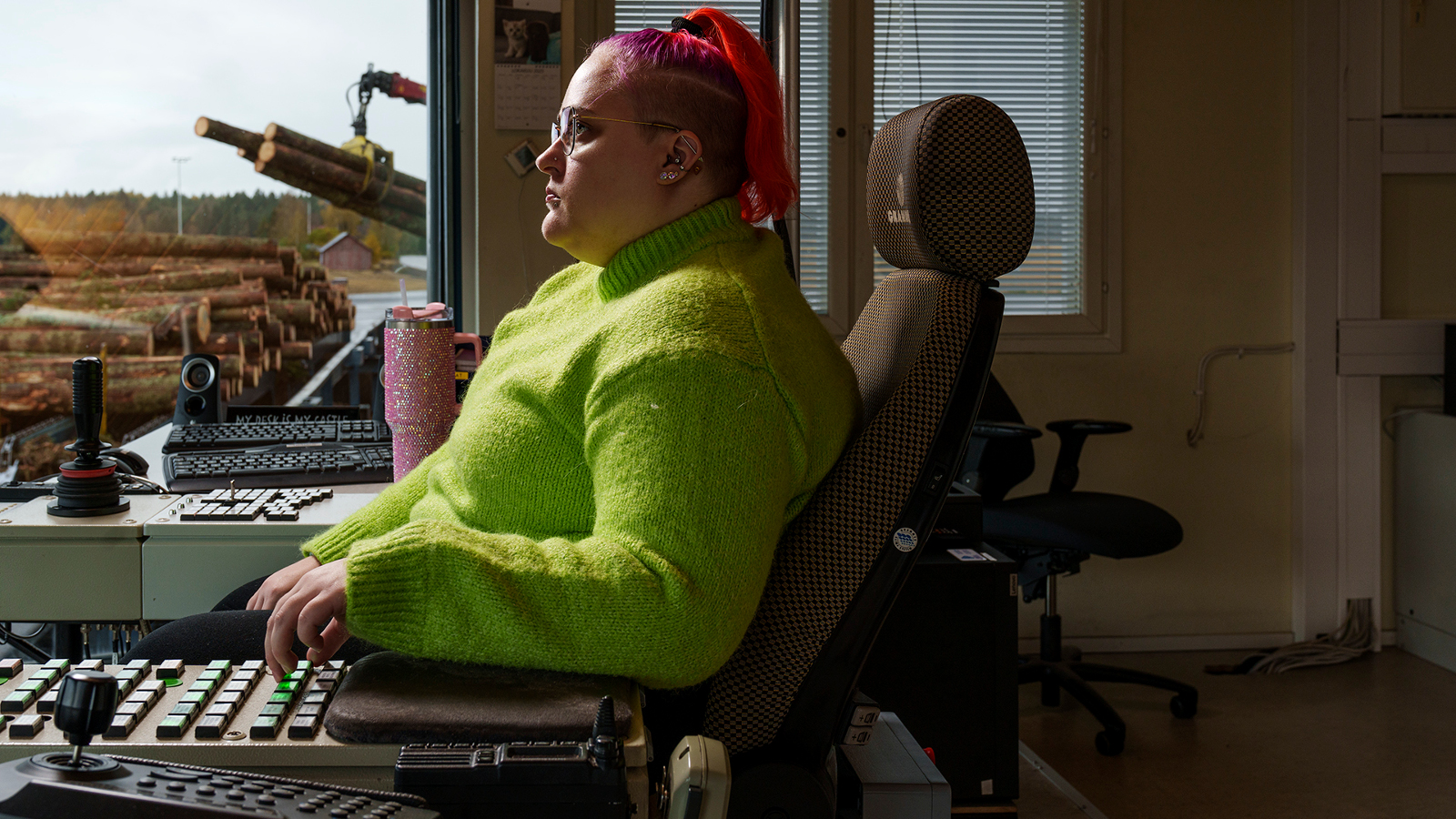 Kuvassa on nuori nainen vaalen vihreässä puserossa istumassa sivuttain nojatuolissa ja hän näppäilee kädellään alla olevia näppäimiä.  Taustalla näkyy ruskeaa maisemaa.