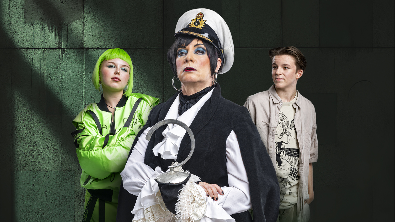 Kuvassa on vasemmalla nuori vaalean vihreässä pusakassa ja hiukset ovat saman väriset. Hänen vieressään on nainen valkoisessa kapteenin hatussa ja mustassa liivissä sekä valkoisessa paidassa. Oikealla on nuori mies harmaassa pusakassa ja lippalakissa.