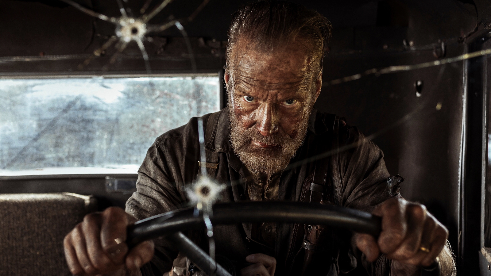 Kuvassa on Jorma Tommila ajamassa sotilasajoneuvoa ja tuulilasissa on luodin reikä. Autossa on tummat seinät ja takaa näkyy avoin ikkuna.