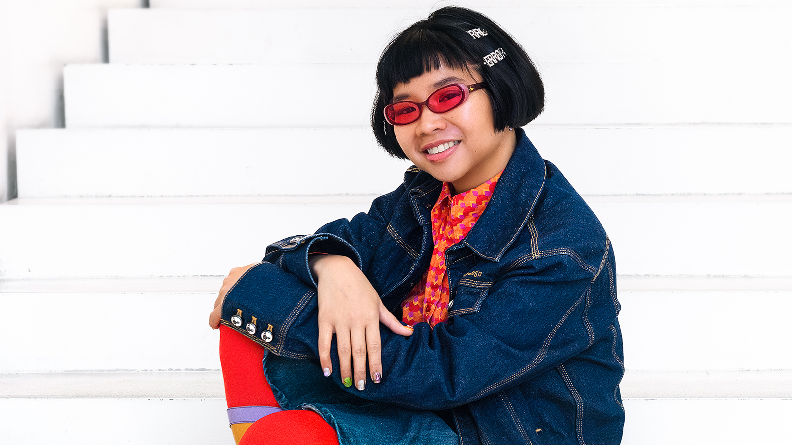 Kuvassa on valkoisilla portailla istumassa Natasha Tontey sinisessä farkkutakissa ja punaisissa sukissa.