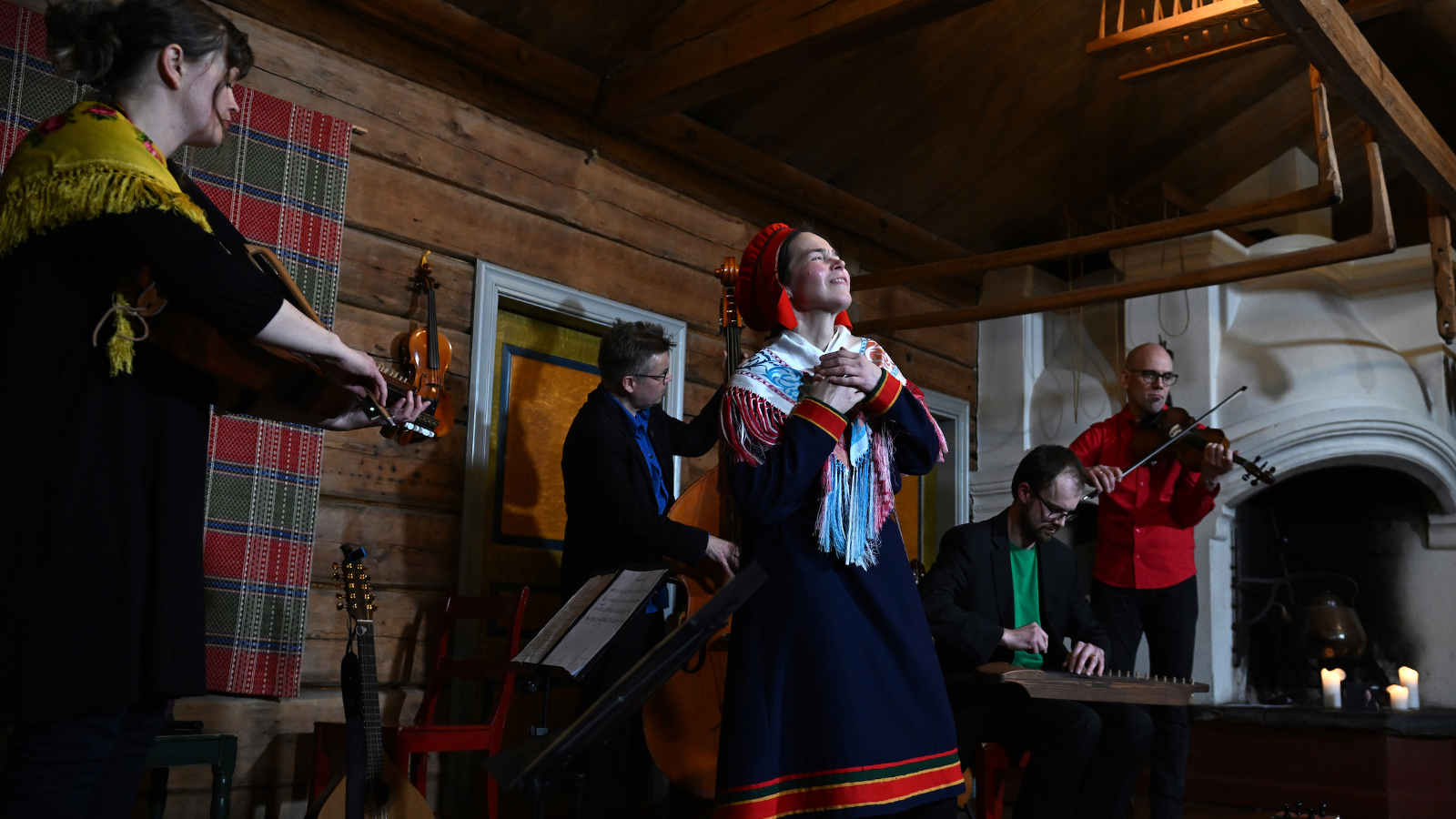  Kuvassa on yläviistoon kuvattu keskellä oleva Anna Morottaja laulamassa Lapin puvussa  ja hänen takanaan on soittamassa  vasemmalla viulua ja taustalla kaksi muuta soittajaa. Taustalla on hirsiseinää.