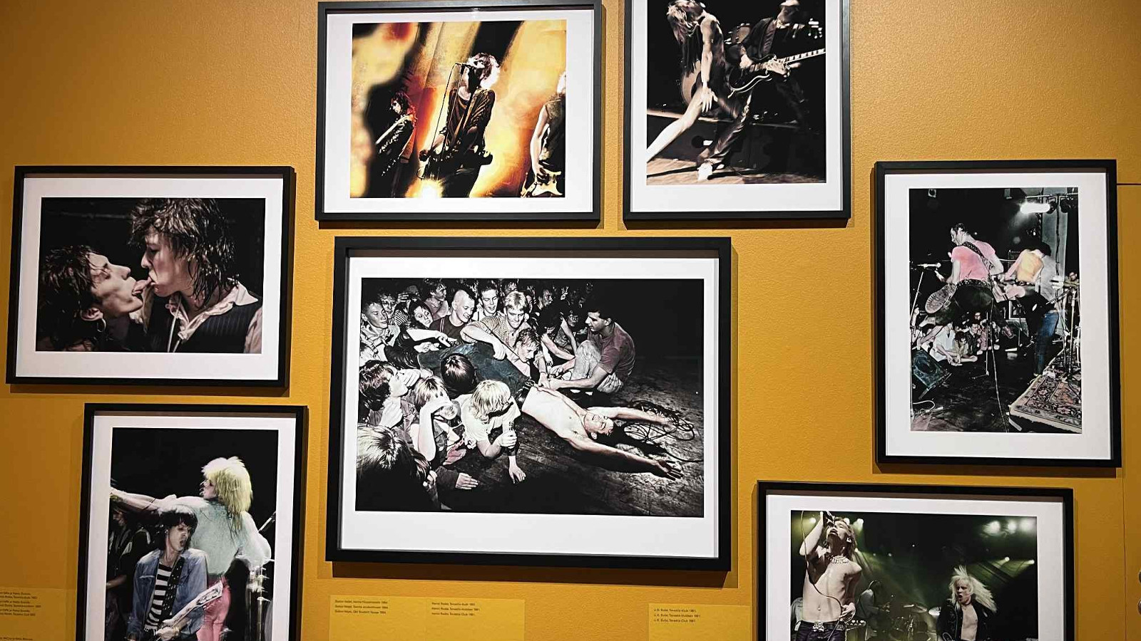 Kuvassa on kellertävällä seinällä musta-valkoisia kuvia. Keskellä olevan ympärillä on kuusi pienempää kuvaa.