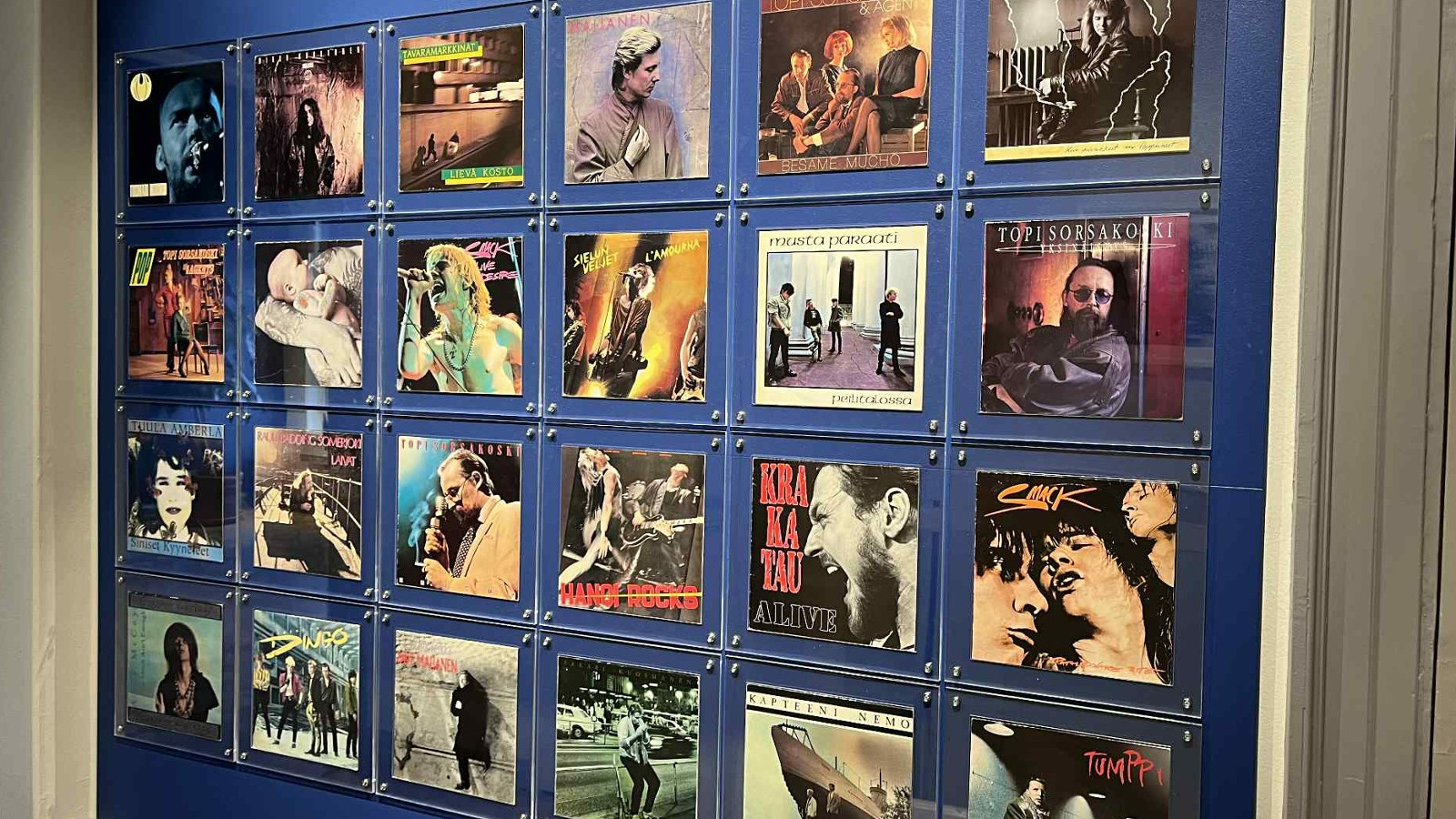 Kuvassa on sinisellä seinällä neljässä rivissä jokaisessa kuusi kuvaa. Kuvat ovat pääosin värillisiä.