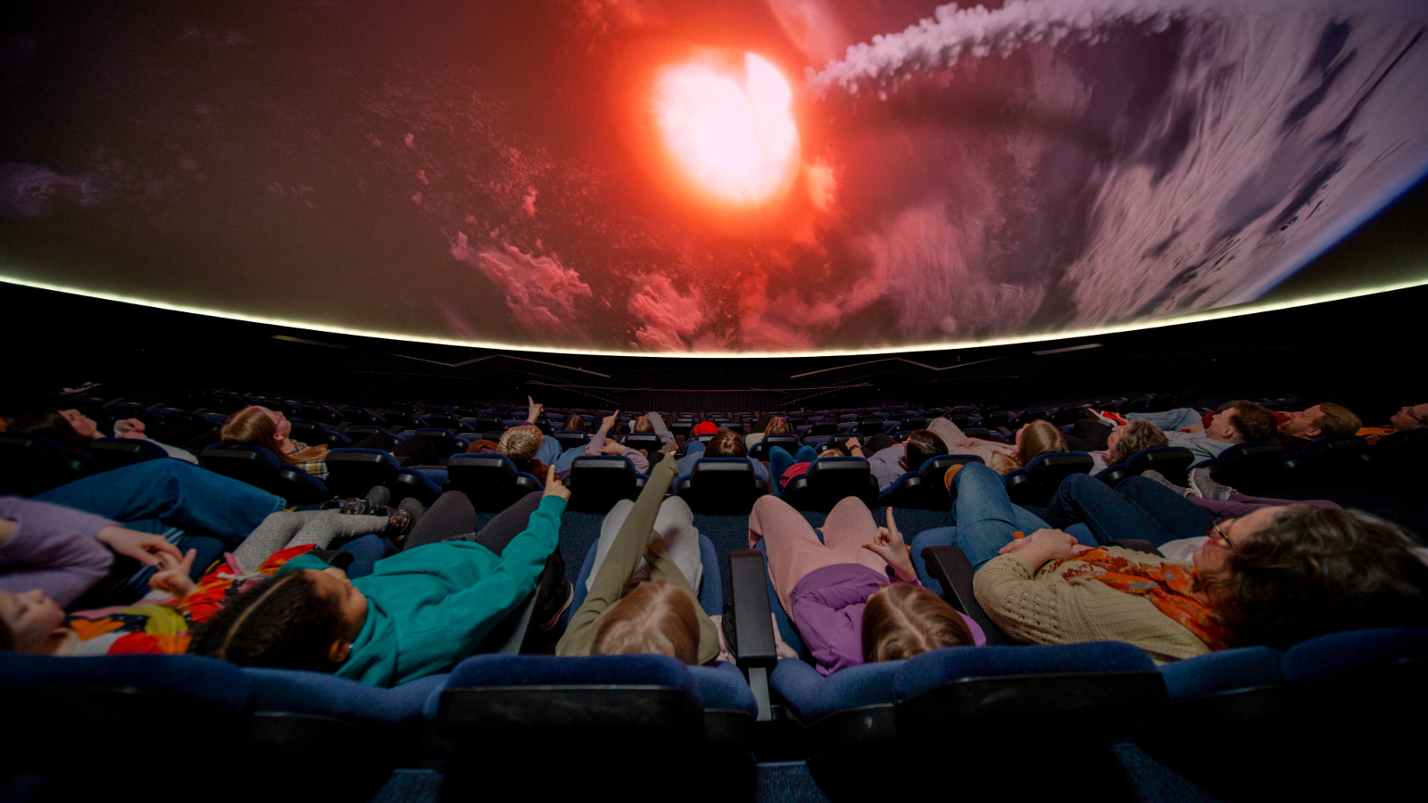 Kuvassa on planetorion lattialla ihmisiä makaamassa pimeässä tilassa ja yläpuolella näkyy punertavaa valoa.