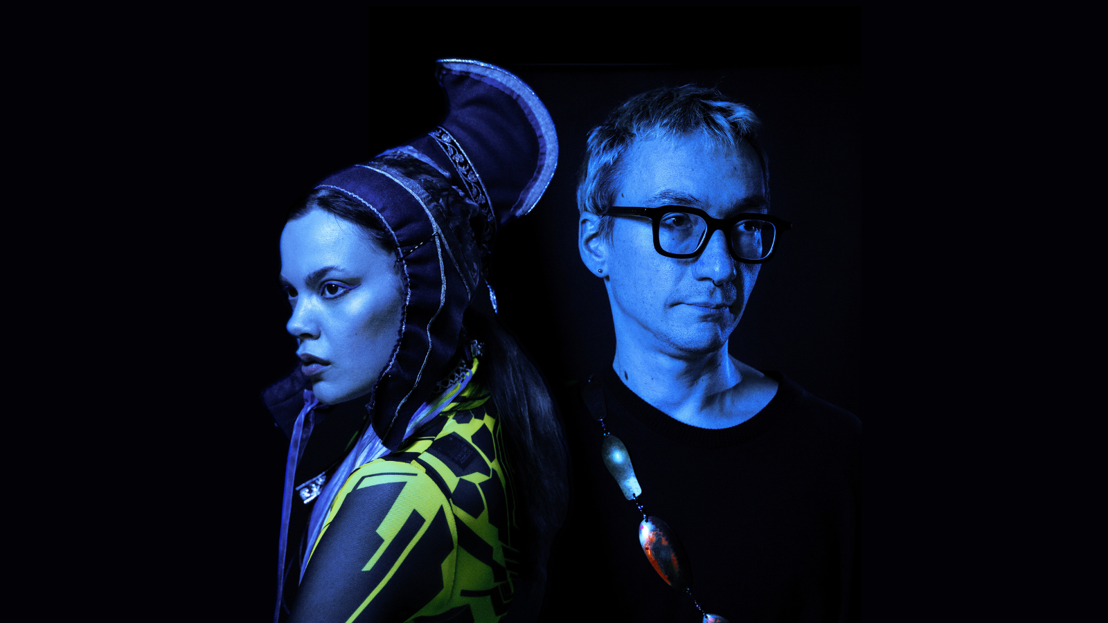 Kuvassa on puolivartalokuvassa vasemmalla Hilda Länsman sivukuvassa ja hänellä on Lapin puvun päähine ja puku. Oikealla on Tuomas Norvio mustassa t-paidassa. Kuvan sävy on tumma.