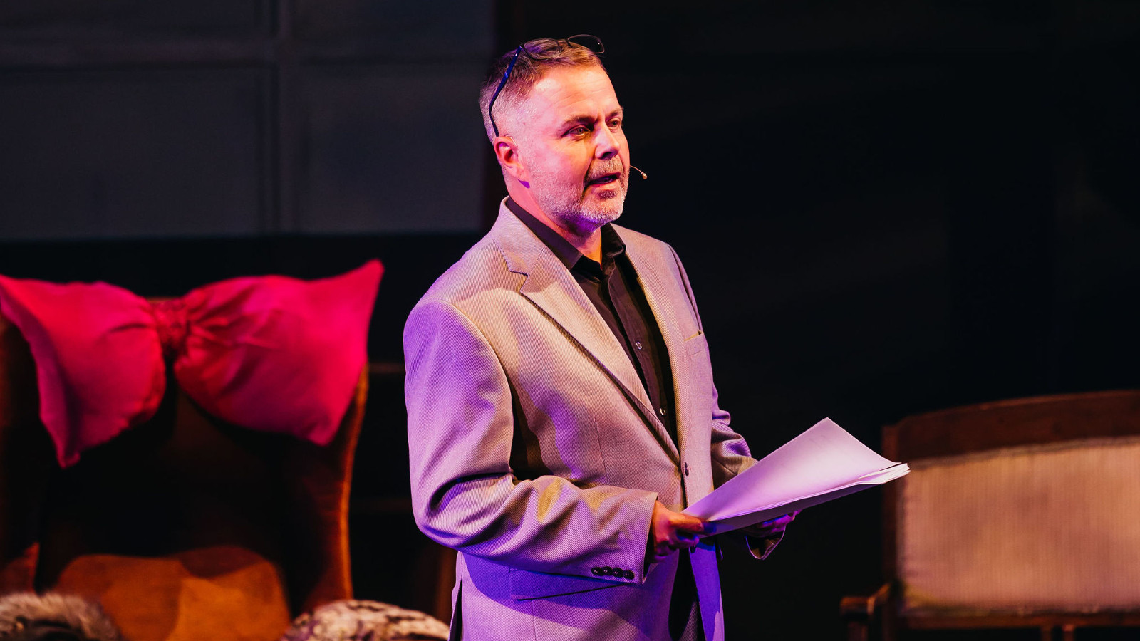 Kuvassa on keskellä Pekka Laasonen seisomassa teatterin penkkien välissä ja seisoo sivuttain. Hänellä on vaalea takki päällään ja käsikirjoitus kädessään. Tausta on tumma.