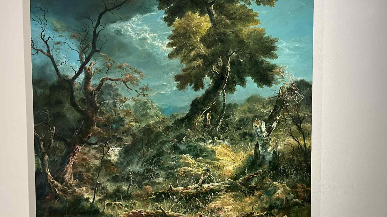 Kuvassa on vakoisessa laatikossa teos, jossa on vasemmalla lehdetön vääntynyt puunrunko ja oikealla vääntynyt runkoinen vihreä puu. Taustalla on sinistä taivasta ja tummia pilviä.