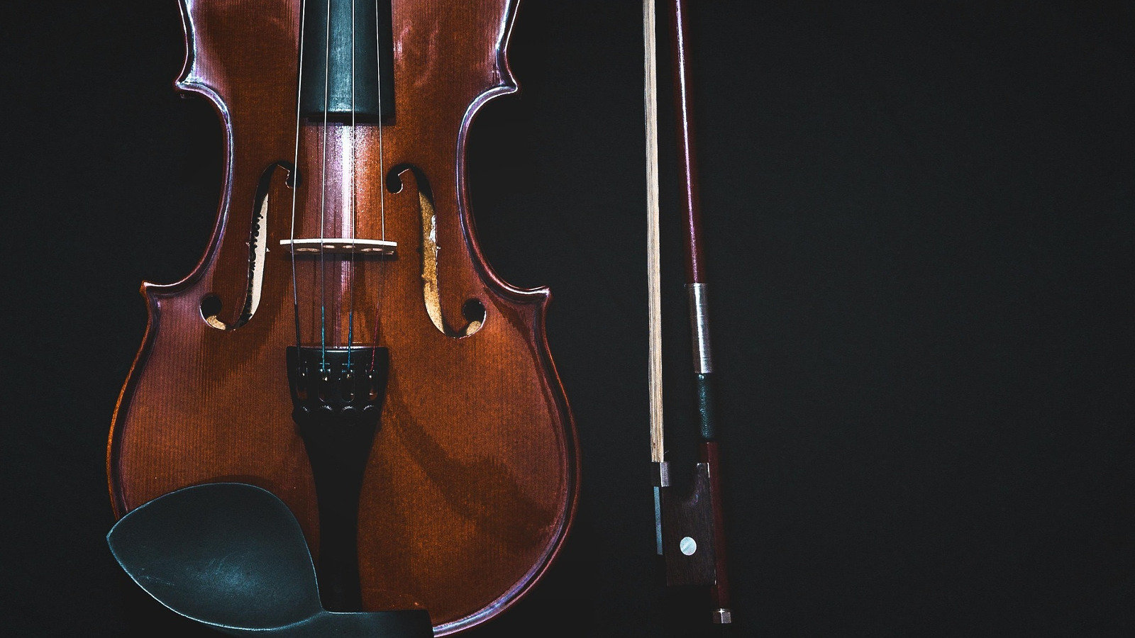 Kuvassa on mustalla pohjalla tumman ruskea viulu pystyssä. 