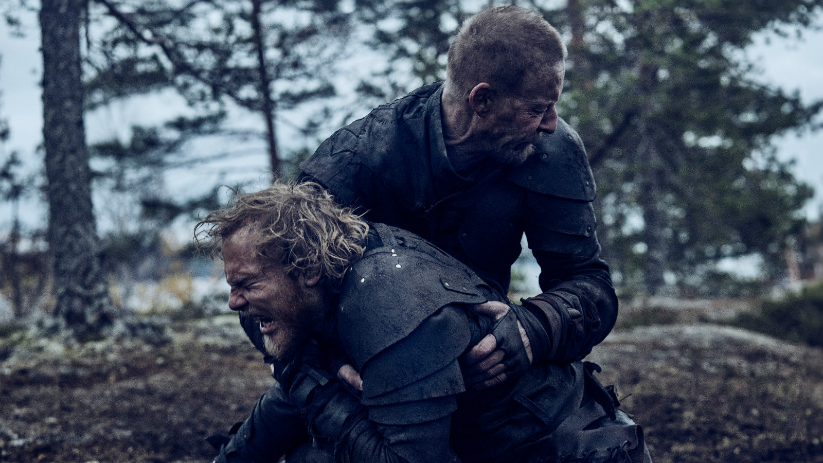 Kuvassa ovat Elias Salonen edessä ja häntä pitää syliotteessa Eero Aho. Taustalla on mäntymetsää.