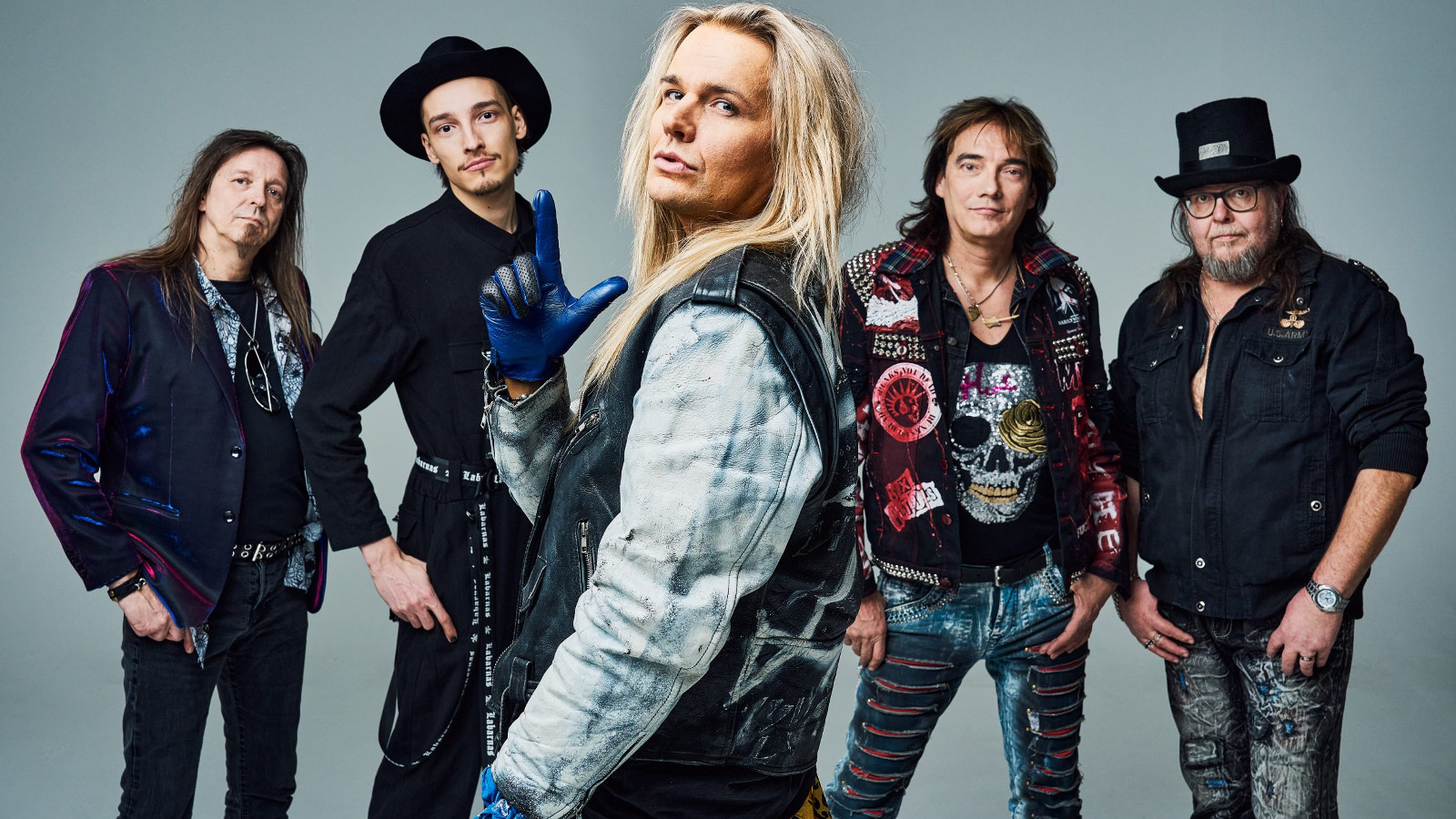 Kuvassa ovat Popedan viisi jäsentä seisomassa. Edessä keskellä on Olli Herman ja hänellä on vaalean sininen farkkupuku. Taaempana toisilla miehillä on mustat vaatteet.