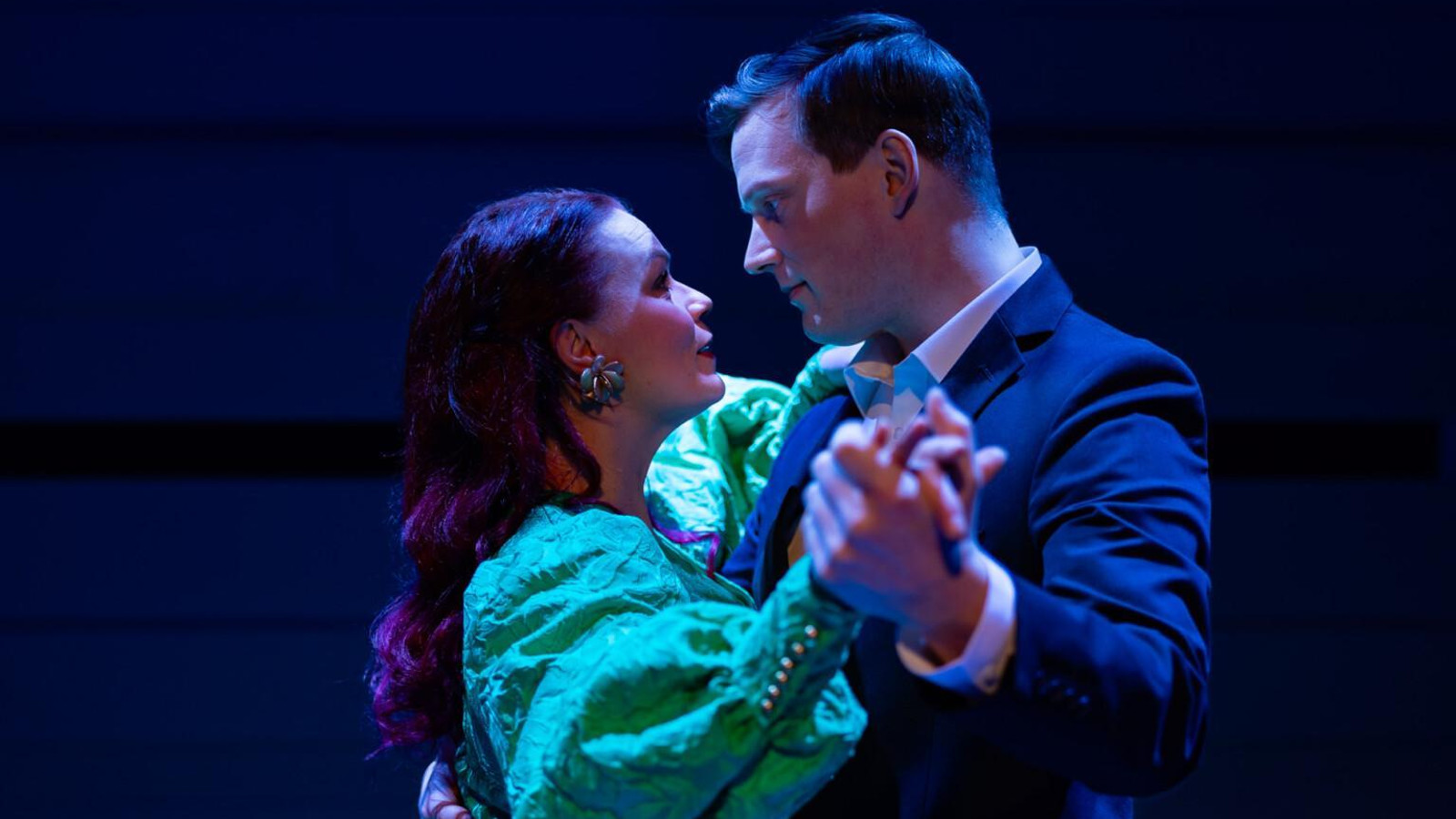 Kuvassa ovat Ella Mustajärvi vaalean vihreässä puhvihihaisessa mekossa ja Juho Markkanen tumman sinisessä takissa puolivartalokuvassa. He ovat vastakkain tanssiasennossa. Tausta on tumma.