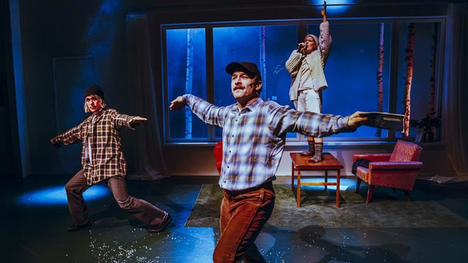 Kuvassa on vasemmalla nuori mies ruutupaidassa tanssiasennossa kädet levitettyinä sivulle ja polvet taivutettuina. Hänellä on ruskea-valkoinen ruutupaita päällään. Keskellä edessä on mies vaalean ruskearuutuisessa paidassa. Taustalla on nuori mies seisomassa tuolin päällä vaaleissa vaatteissa. Taustalla on ikkuna ja kuvan sävy on tumman sininen.