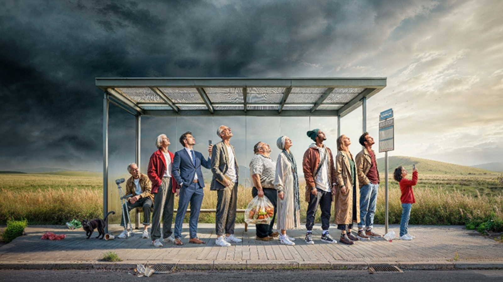 Kuvassa on ihmisiä bussipysäkillä, jossa on valokate.  Kaikki katsovat taivaalle, jossa on tummaa pilveä ja vaalenvaa taivasta oikealla. Taustalla on keltaista viljapeltoa.