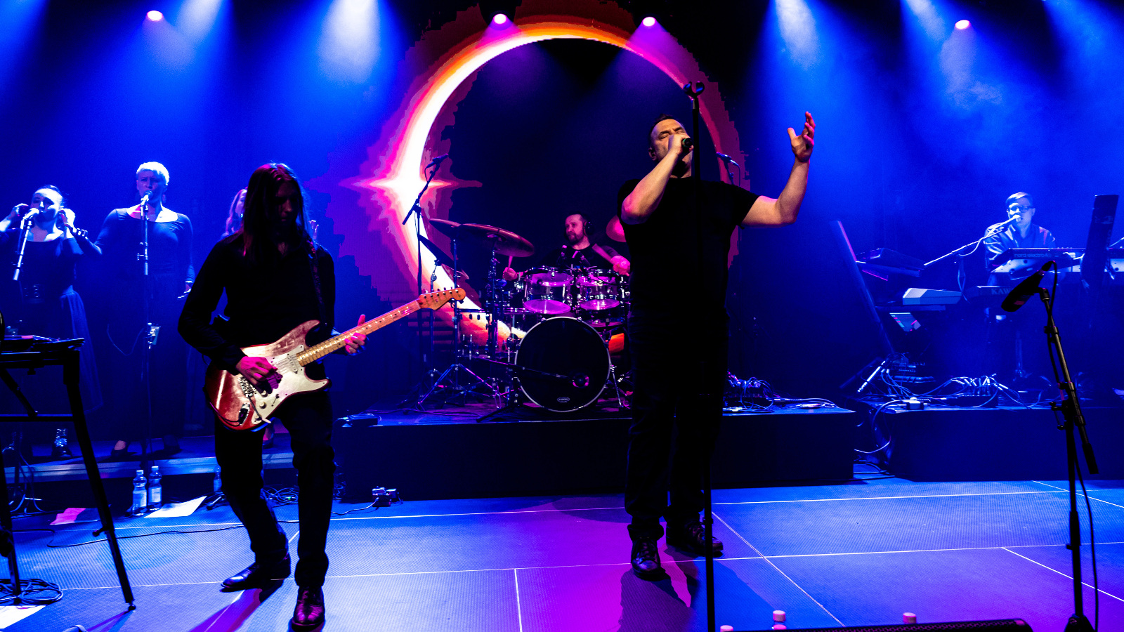 Kuvassa on Pulsa-yhtyeen kaksi jäsentä ja vasemman puoleinen soittaa kitaraa.  Keskellä on laulaja tummassa asussa. Taustalla on sinistä valoa  ja keskellä valoympyrä.