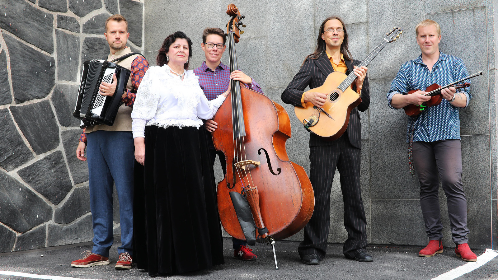 Kuvassa on yhtye Hilja Grönfors & Latso Dzinta seisomassa ja toisena vasemmalta on Hilja Lindfors mustalaisasussa, mustassa pitkässä puolihameessa ja valkoisessa puserossa.  Vasemmalla on mies, jolla on harmonikka rinnallaan ja keskellä on mies edessään basso. Hänen vieressään oikealla on mies kitara kädessään ja oikealla mies viulu kädessään. Taustalla on harmaata liuskekiveä ja harmaata seinää.