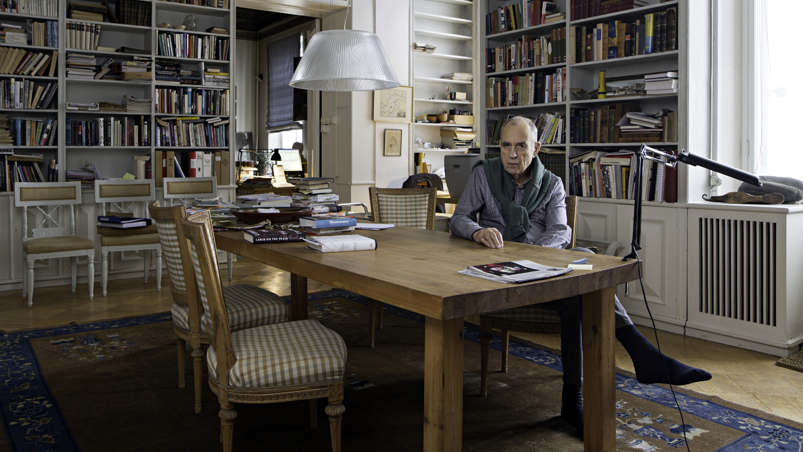 Kuvassa on Jörn Donner ruskean kirjoituspöydän ääressä ja taustalla on kirjahyllyjä täynnä kirjoja.