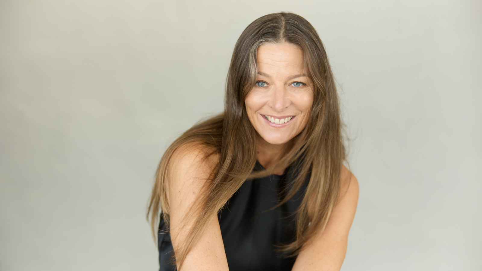 Kuvassa on Mia Hafrén puolivartalokuvassa. Hänellä on pitkät ruskeat hiukset ja musta hihaton t-paita. Tausta on harmahtava.