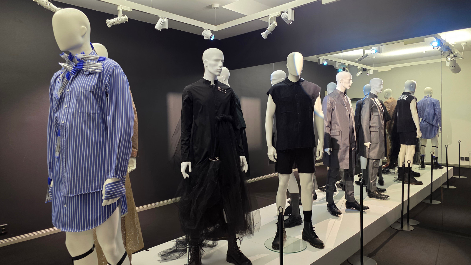 Kuvassa on miesmallinukkeja ja vasemmalla on sinipaitainen mallinukke. Muut ovat rivissä mustissa ja ruskehtavissa väreissä.