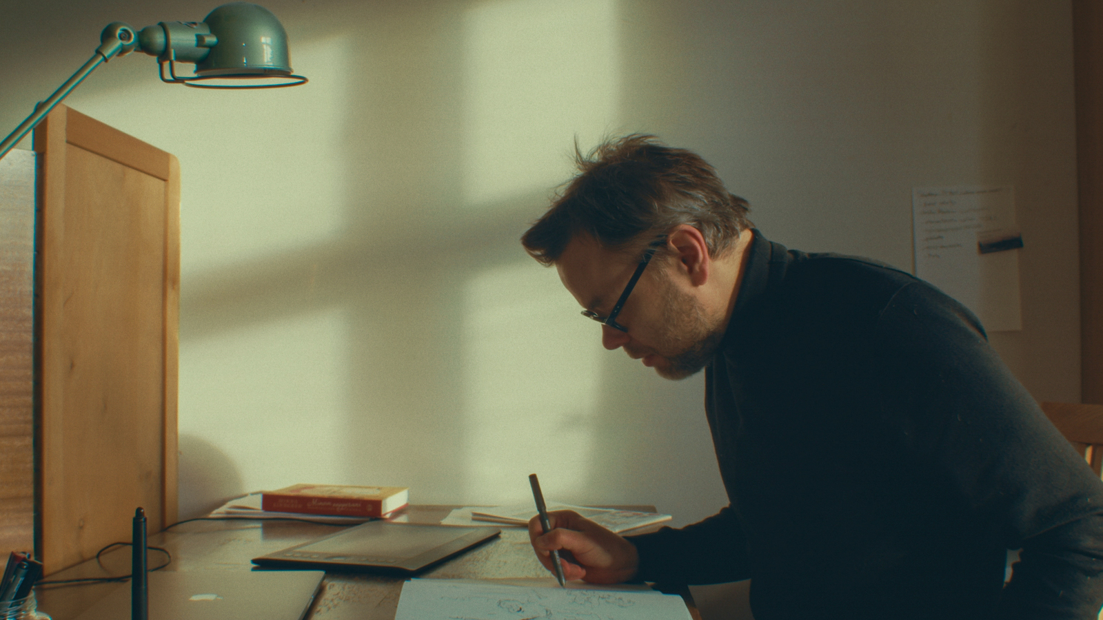 Kuvassa on sivuttain Ville Ranta piirtämässä pöydän ääressä puolivartalokuvassa. Edessä on ruskea taulu.