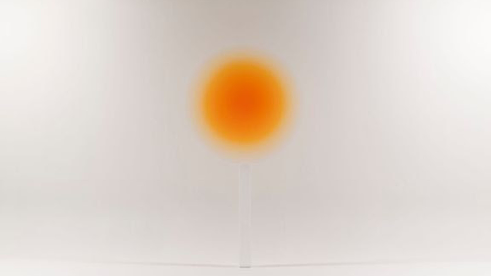 Kuvassa on vaalean harmaalla pohjalla sumean oranssi aurinko keskellä.