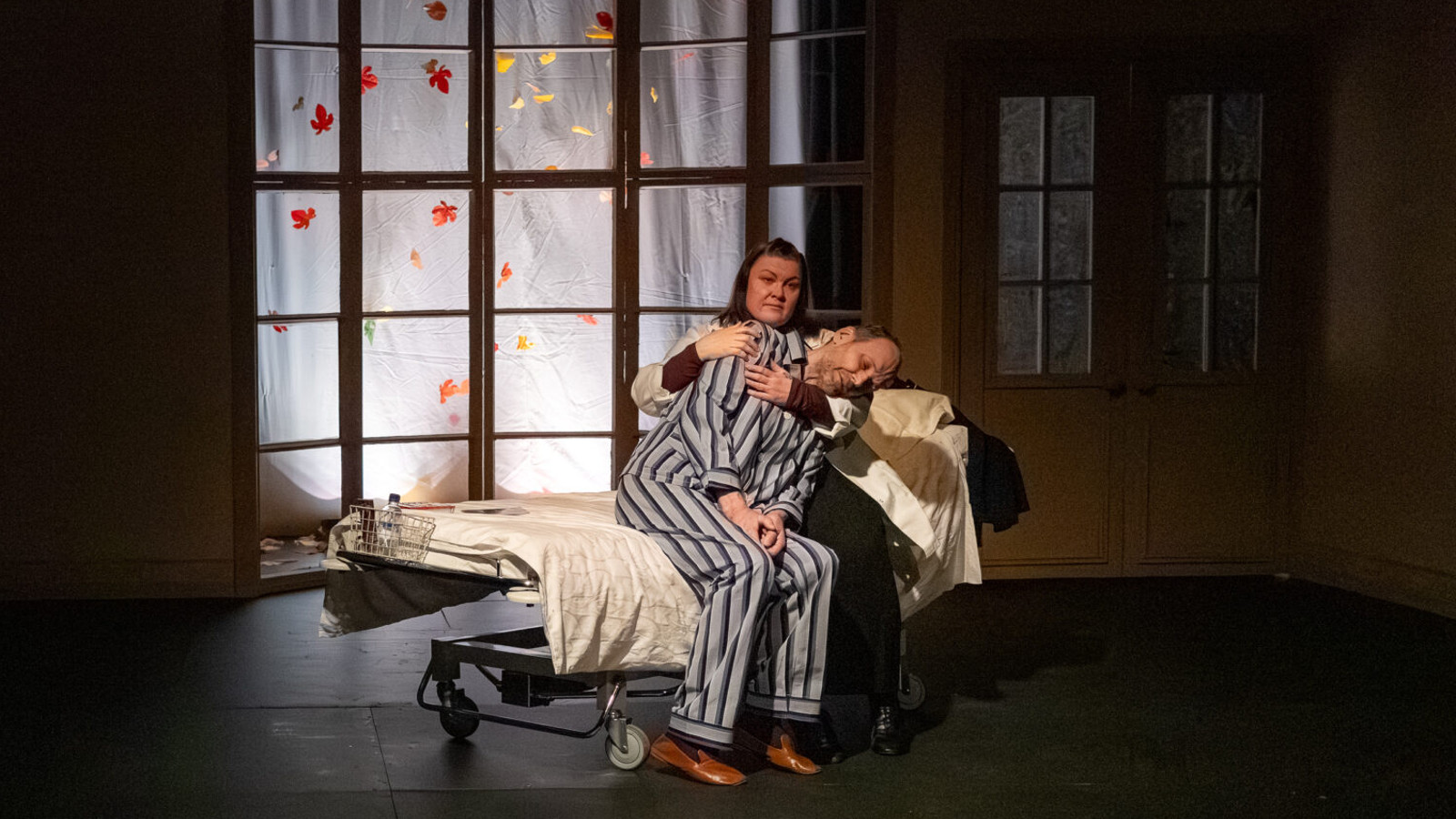 Kuvassa on sairaalasängyn päällä mies raidallisessa pyjamassa ja hän nojaa takanaan istuvaan naiseen.    