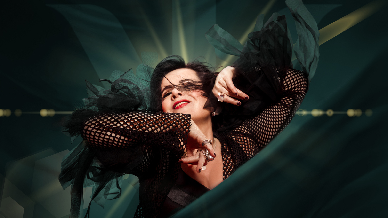 Kuvassa on Kaija Koo puolivartalokuvassa ja hänellä on kädet kohotettuina vauhdikkaasti. Hänellä on musta puku ja hihat ovat verkkomaiset. Tausta hihreän tumma ja valoa tulee pään yläpuolelta.