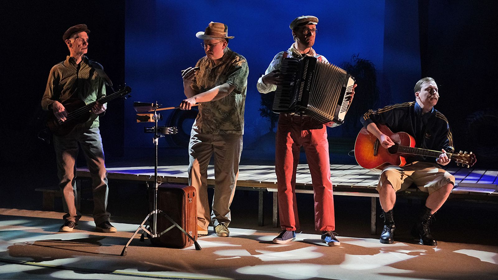 Kuvassa on neljän miehen bändi. Vasemmalla on kitaristi vieressään huuliharpisti ja oikealla hanuristi ja oikealla istumassa terassin reunalla kitaristi soittamassa akustista kitaraa.