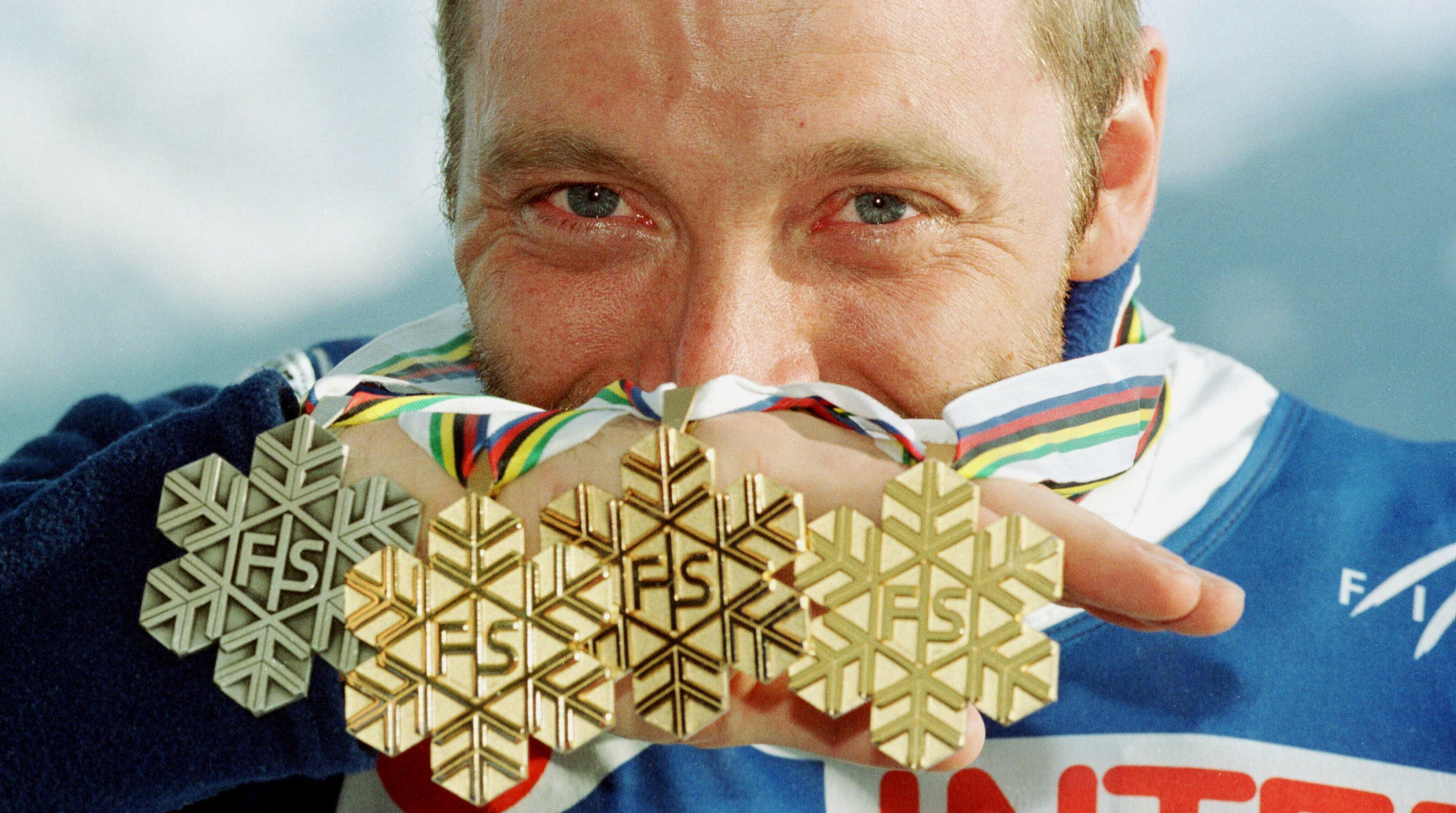 Kuvassa on taustalla Mika Myllylän kasvot ja hän pitää puoliksi kasvojen edessä neljä mitalia, joissa on havukuviota ja keskellä kirjaimet FS. taustalla vaalean sinistä pilveä.