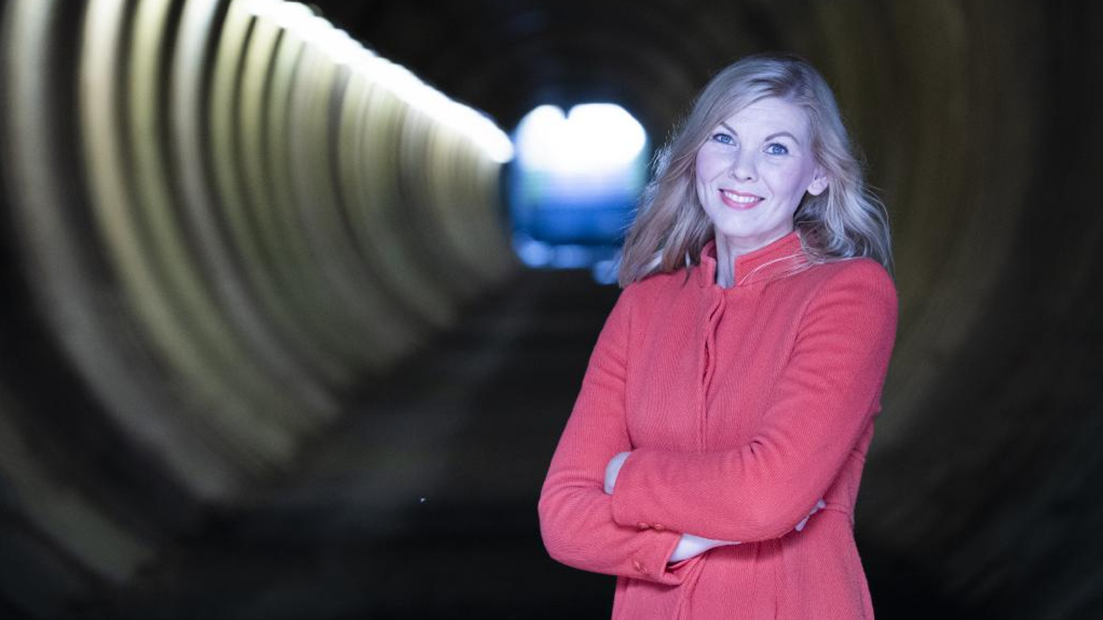 Kuvassa on oikealla pinkissä jakussa Minna Leinonen seisomassa. Taustalla on näkyy tunnelia ja vasemmalla tunnelin valoja. 