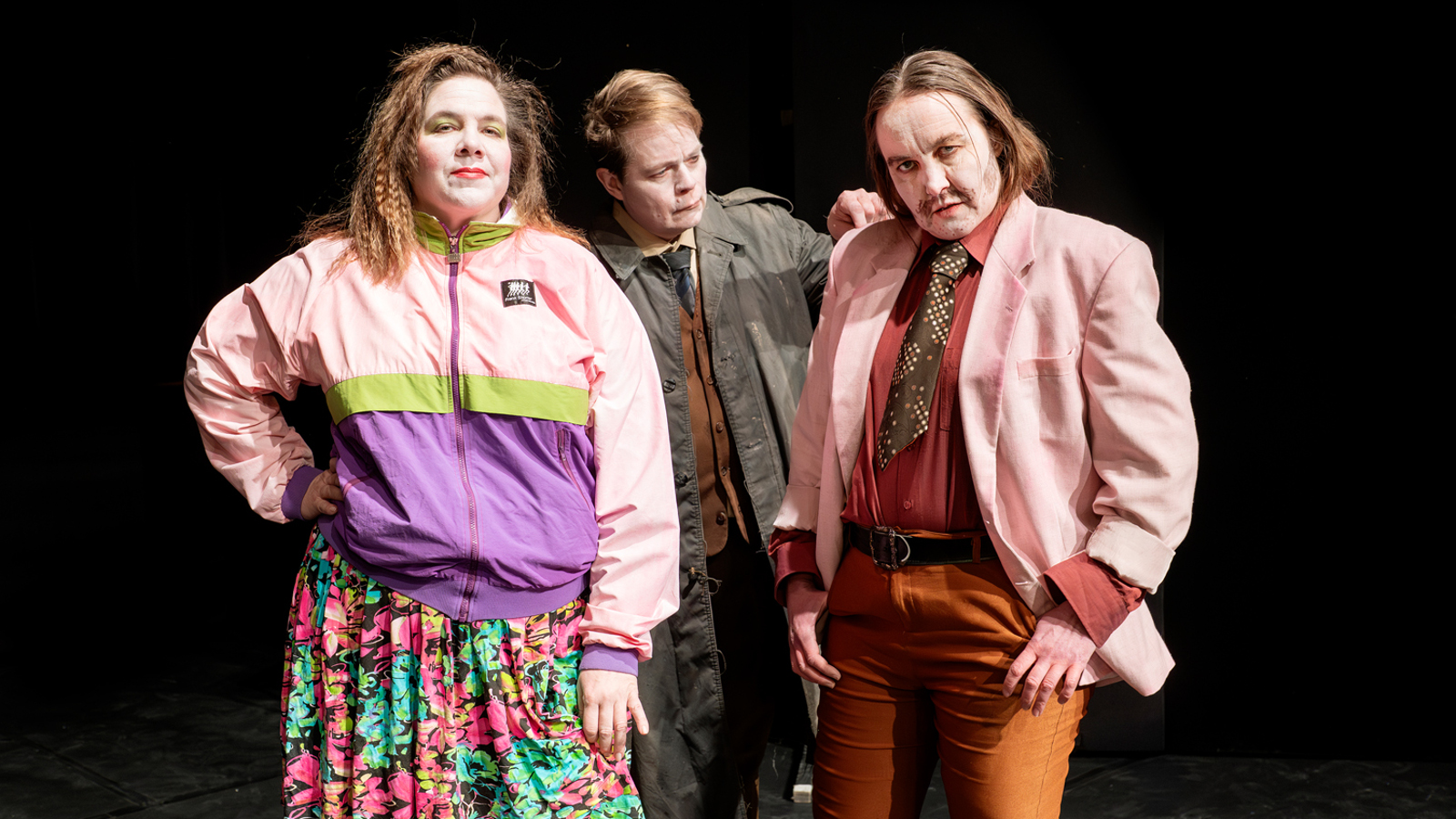 Kuvassa on vasemmalla nainen vaalean puna-lilassa pusakassa ja kukallisessa puolihameessa. Keskellä on mies ruskeassa päällystakissa ja oikealla on mies vaalean punaisessa takissa ja ruskeissa housuissa.