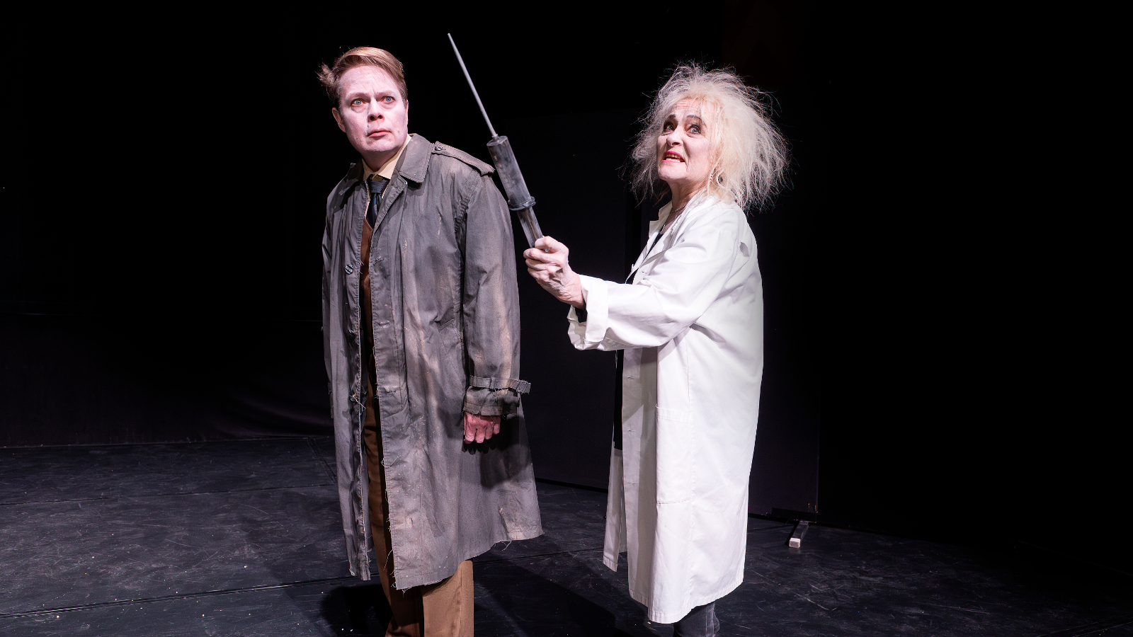 Kuvassa on mies ruskeassa päällystakissa ja oikealla nainen vakoisessa päällystakissa. Tausta on tumma.