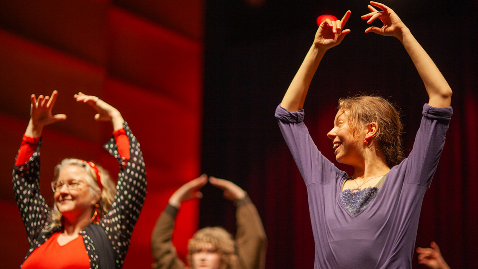 Kuvassa on puolivartalokuvassa kolme flamenco-tanssijaa ja heillä on kädet ylhäällä. Taustalla on punertavaa seinää.