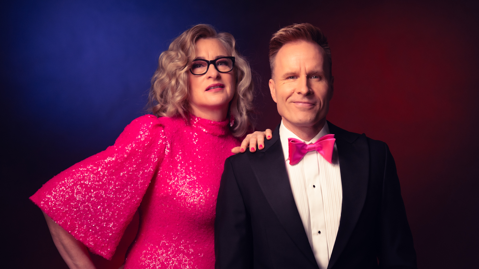 Kuvassa on vasemmalla Katja Ståhl pinkissä, glittermekossa, jossa on leveä hihat. Hän pitää vasenta kättään Mikko Kekäläisen olkapäällä, jolla on musta takki, valkoinen paita ja pinkki rusetti. He ovat puolivartalokuvassa. Tausta on tummansininen.