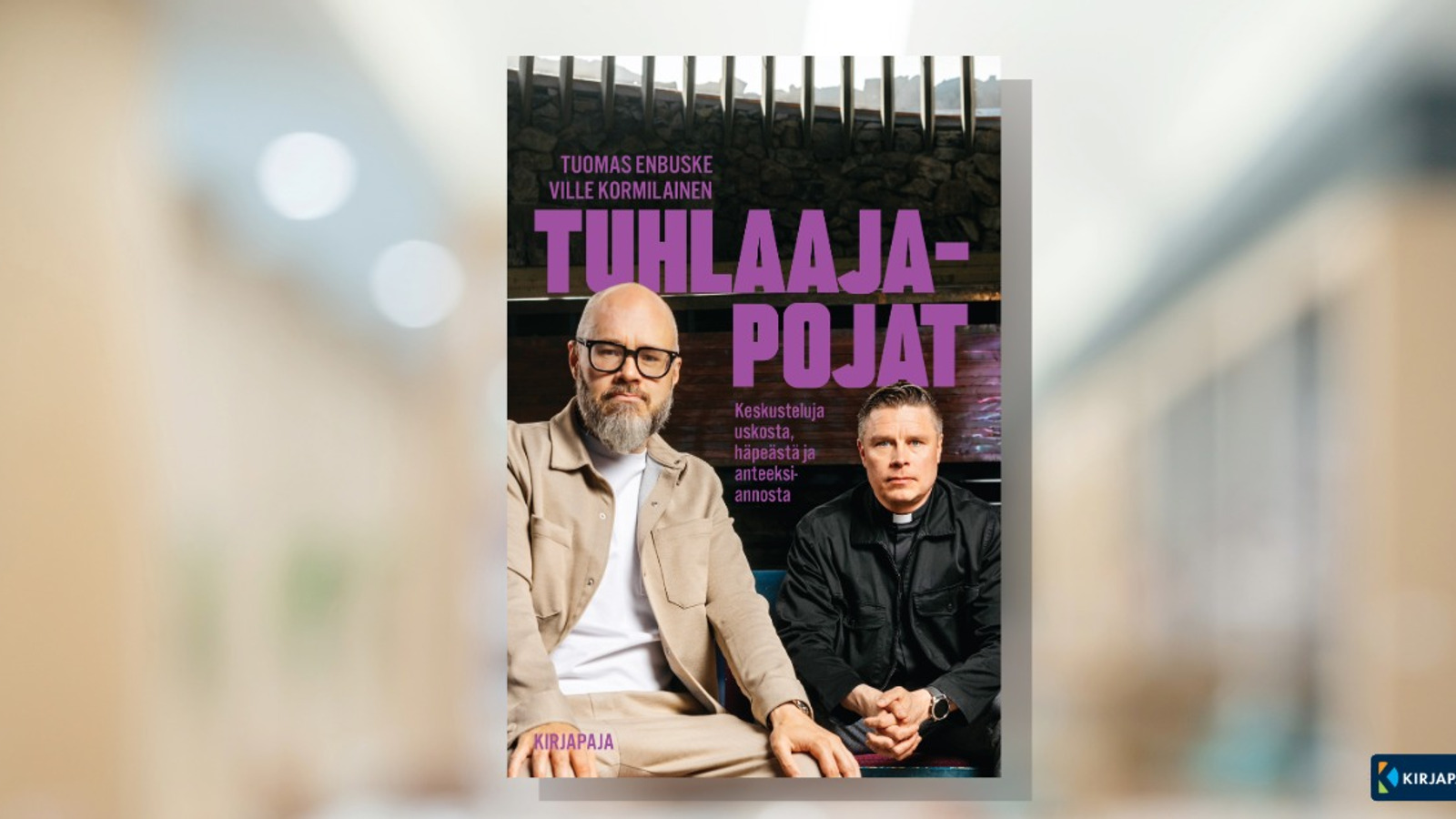 Kuvassa on vaalean ruskealla utuisella pohjalla kirjan kansi. Siinä ovat istumassa vasemmalla vaalean ruskeassa puvussa Tuomas Enbuske ja oikealla taaempana ville Kormilainen mustassa puserossa. Takana on isoin violetein kirjaimin kirjan nimi Tuhlaajapojat.