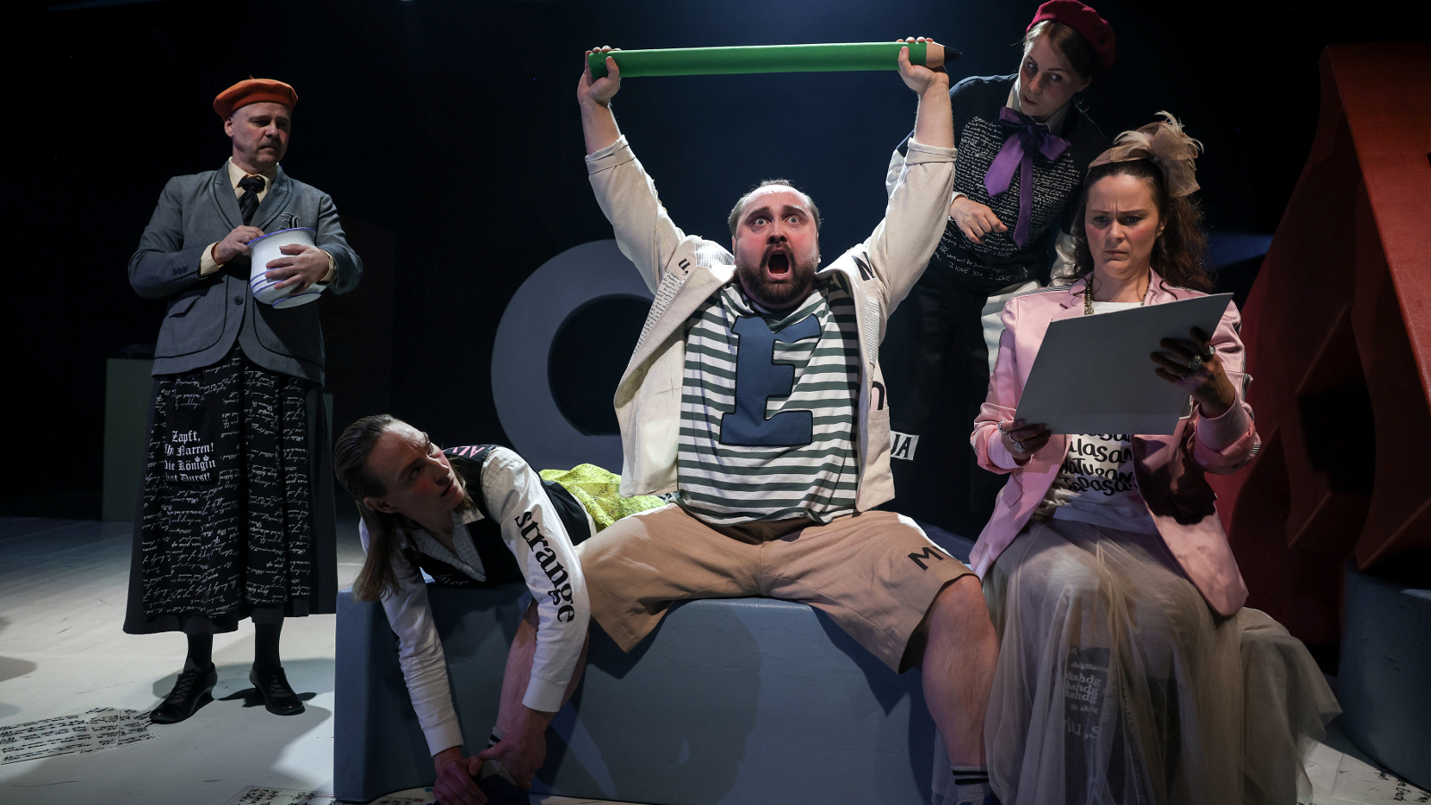 Kuvassa on keskellä Sami Sainio, joka istuu sohvalla ja pitää vihreää keppiä ylhäällä käsissään.  Vieressä istuu nainen vaaleassa takissa. Hänellä on kansia kädessään. Taustalla seisoo harmaassa takissa nainen.