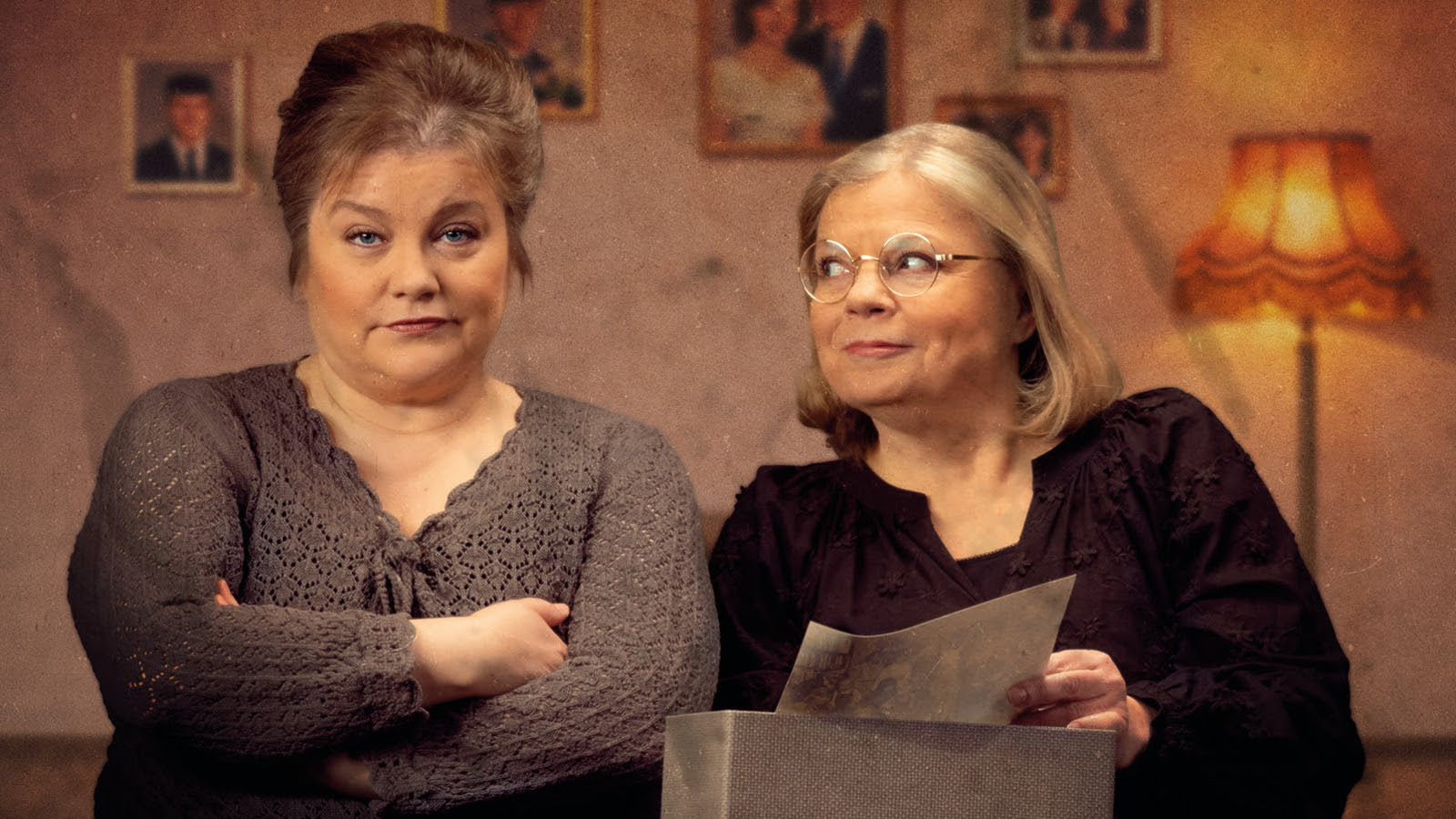 Kuvassa on vasemmalla nainen ruskeassa villapuserossa kädet puuskassa. Oikealla on nainen mustassa puserossa ja hän katsoo vasemmalla olevaa. Taustalla on huonetta.