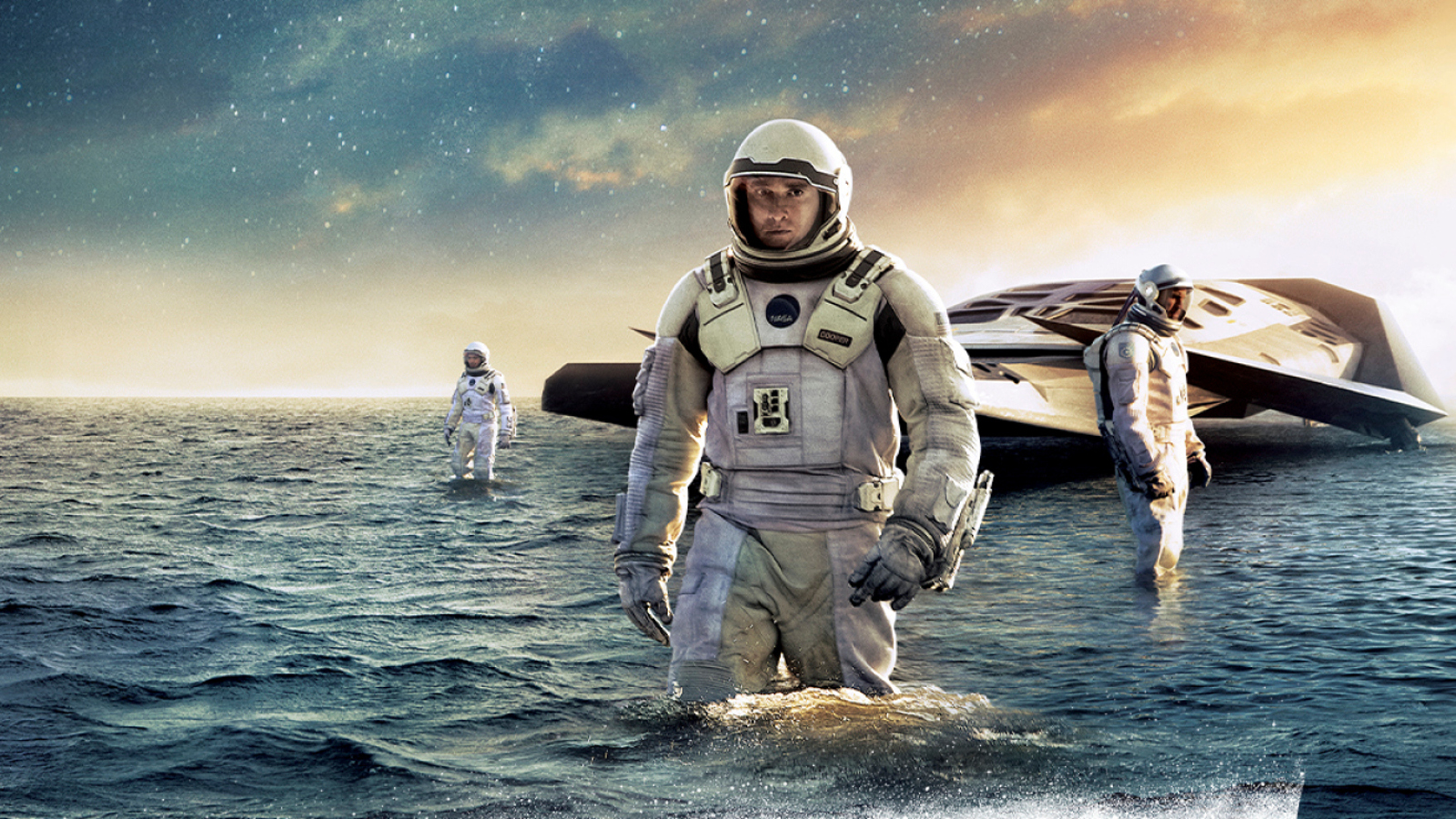 Kuvassa on keskellä vaaleassa avaruuspuvussa ja kahlaa vedessä. Taaempana kahlaa toinen avaruuspukuinen henkilö. Takana on vedessä on litteä alus ja sen edessä on kolmas henkilö. Yllä on tumman sinistä pilveä, joka heijastuu tumman siniseen veteen