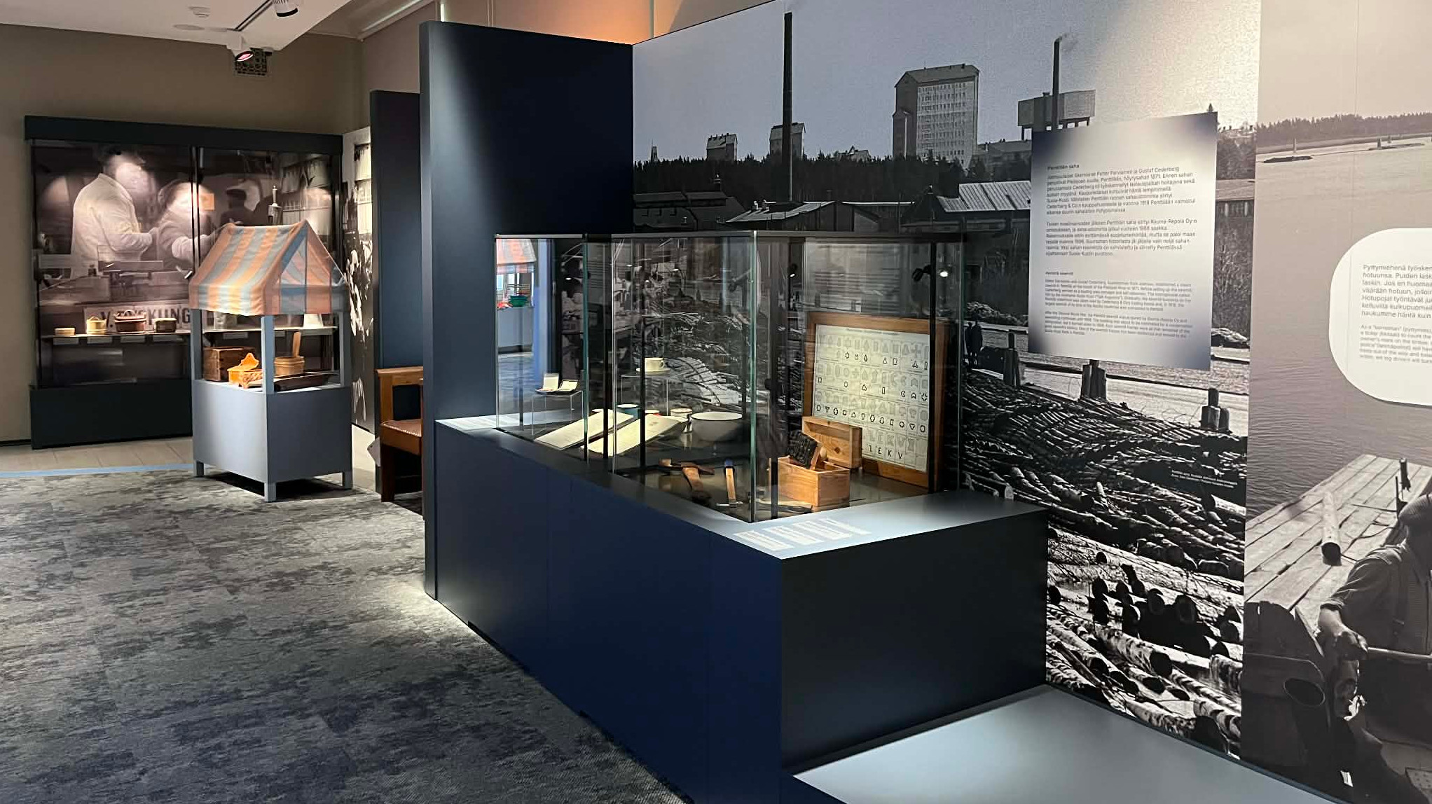 Kuvassa on museosalin vitriinejä, joissa on mustalla jalustalla. Taustalla on takaseinällä ja oikealla seinällä isoja valokuvia. 