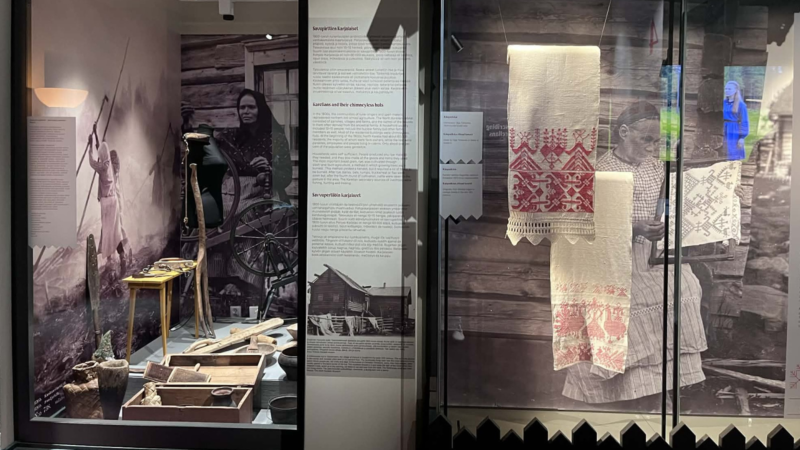 Kuvassa on vasemmalla seinällä ja takana mustavalkokuvia koskenlaskusta ja vanhan talon seinustalta. Oikealla on roikkumassa valkoisia liinoja ja käsitöitä, joissa on punaista kirjontaa.